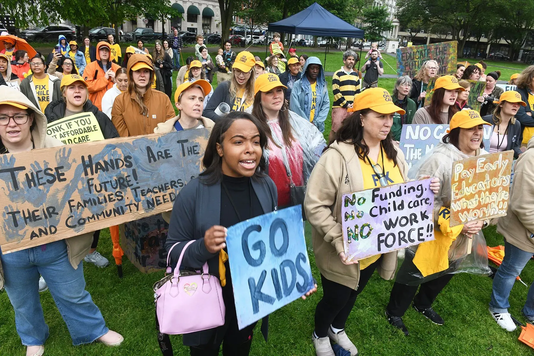 حشد من المتظاهرين يرتدون قبعات صفراء، يحملون لافتات تدعو لتحسين رعاية الأطفال وزيادة أجور المعلمين في حدث لدعم حقوق الأطفال.