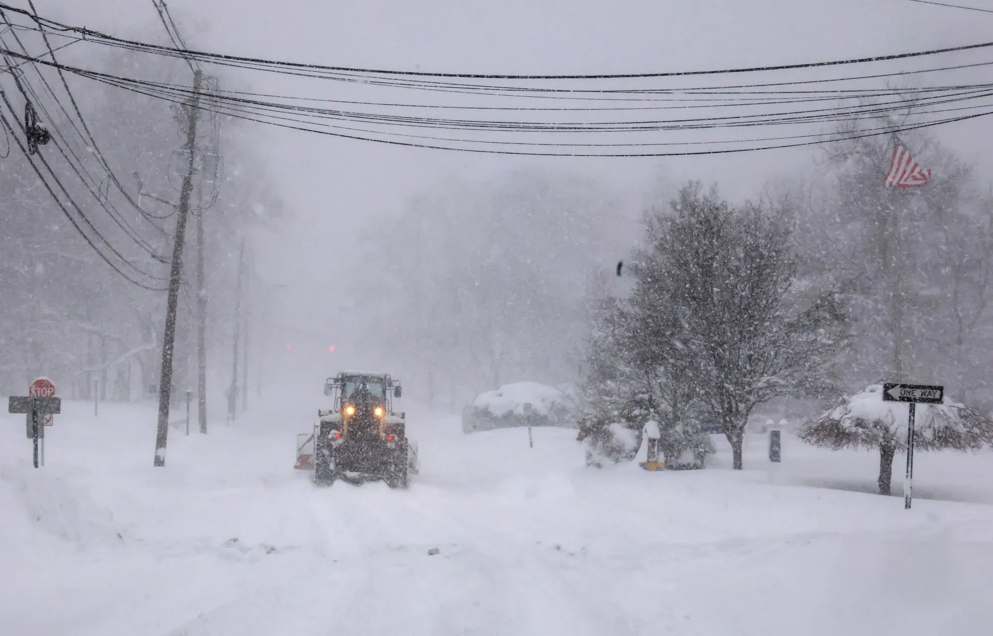 عاصفة ثلجية قوية تجتاح منطقة حضرية، مع تراكم الثلوج والرياح العاتية، مما يعيق حركة المرور ويظهر جهود إزالة الثلوج.