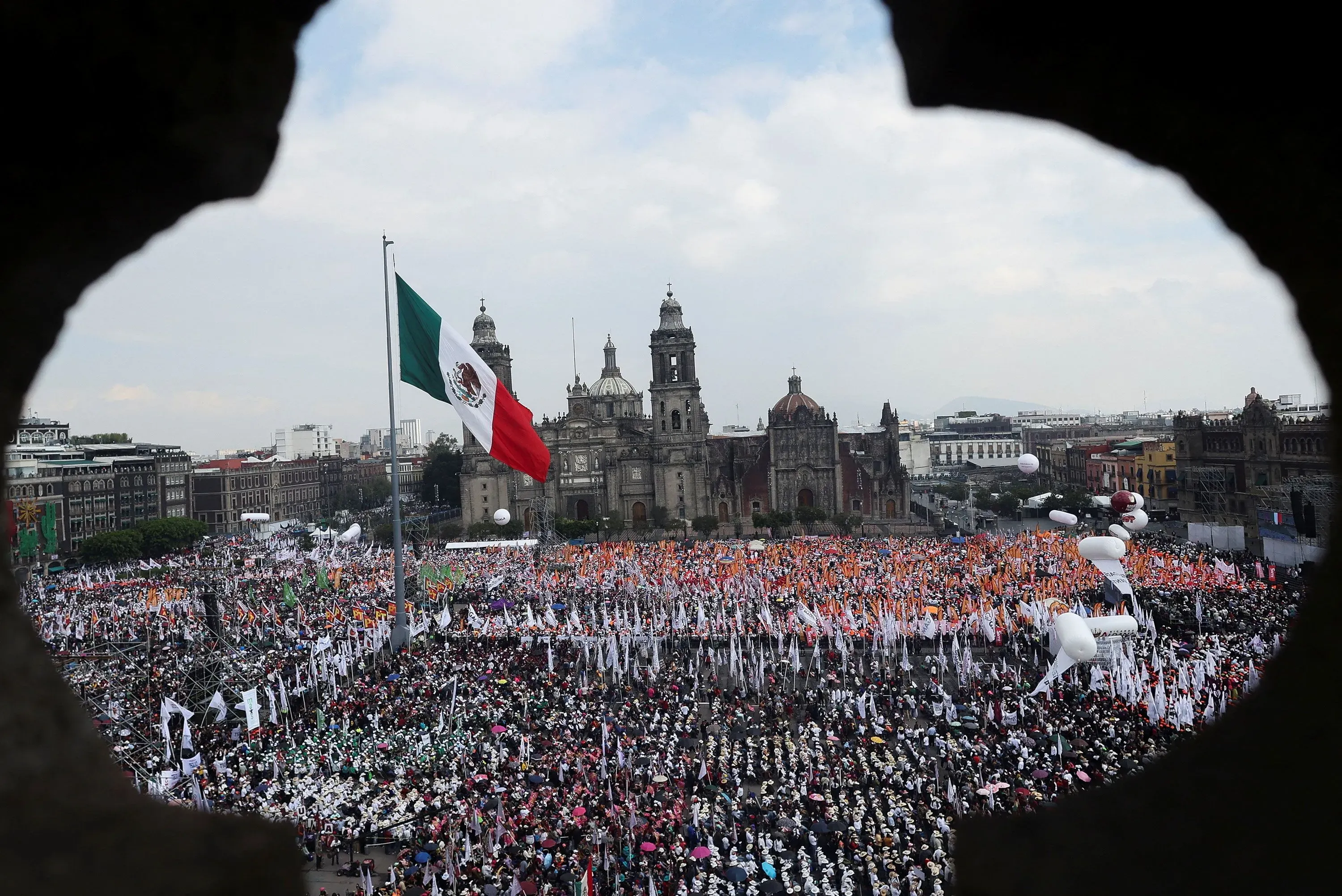 تجمع حاشد في ساحة زوكالو بمكسيكو سيتي، يظهر العلم المكسيكي مع خلفية معمارية تاريخية، مشيراً إلى دعم شعبي قوي لكلوديا شينباوم.