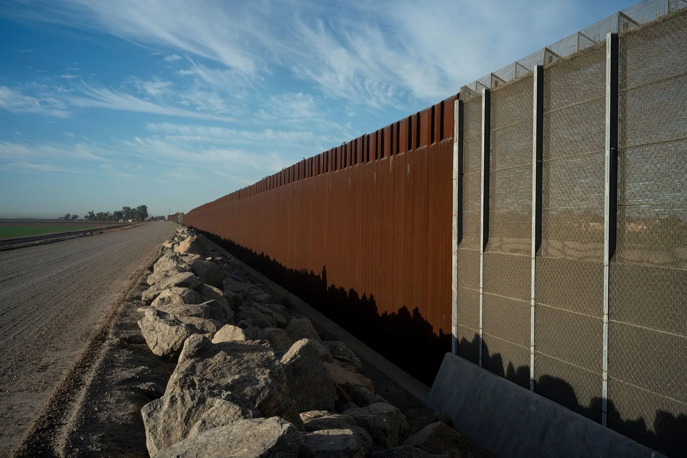 جدار فاصل على الحدود بين الولايات المتحدة والمكسيك، يمتد على طول طريق ترابي محاط بالصخور، يعكس قضايا الهجرة في منطقة أريزونا.