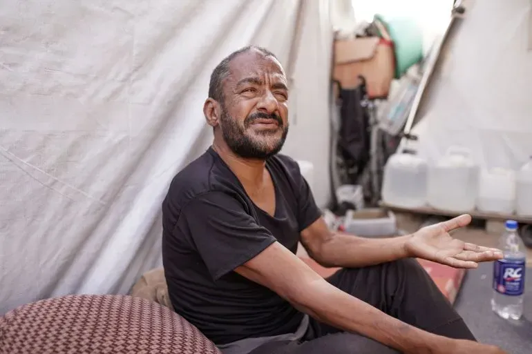 رجل يجلس في خيمة مؤقتة، يعبر عن معاناته من الظروف الصعبة في غزة، حيث تزداد مشاكل الجرذان مع تدهور الأوضاع.