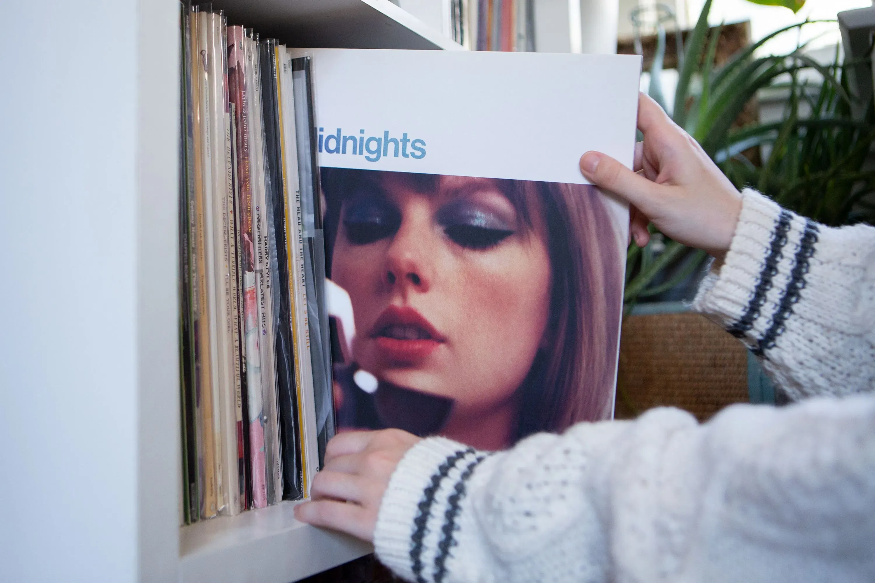 يد تظهر يد شخص يختار أسطوانة "Midnights" لتايلور سويفت من مجموعة أسطوانات فينيل، مع خلفية تحتوي على أسطوانات أخرى.