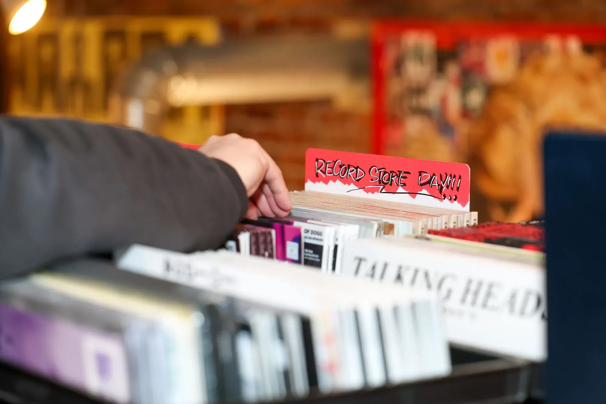 يد تظهر يد شخص تبحث بين أسطوانات الفينيل في متجر، مع لافتة تشير إلى "يوم متجر الأسطوانات"، مما يعكس اهتمام الجيل Z بالثقافة الموسيقية.