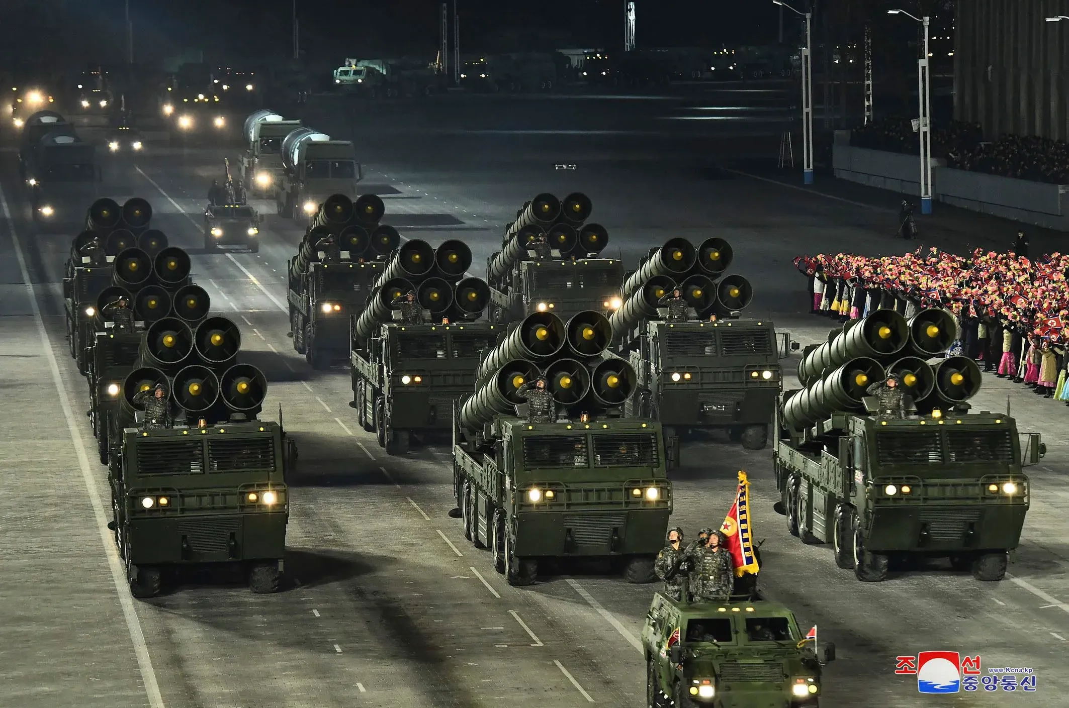 عرض عسكري في كوريا الشمالية يظهر مركبات عسكرية مسلحة بصواريخ، مع حشود من الناس في الخلفية، في سياق مناقشة التجارب النووية.