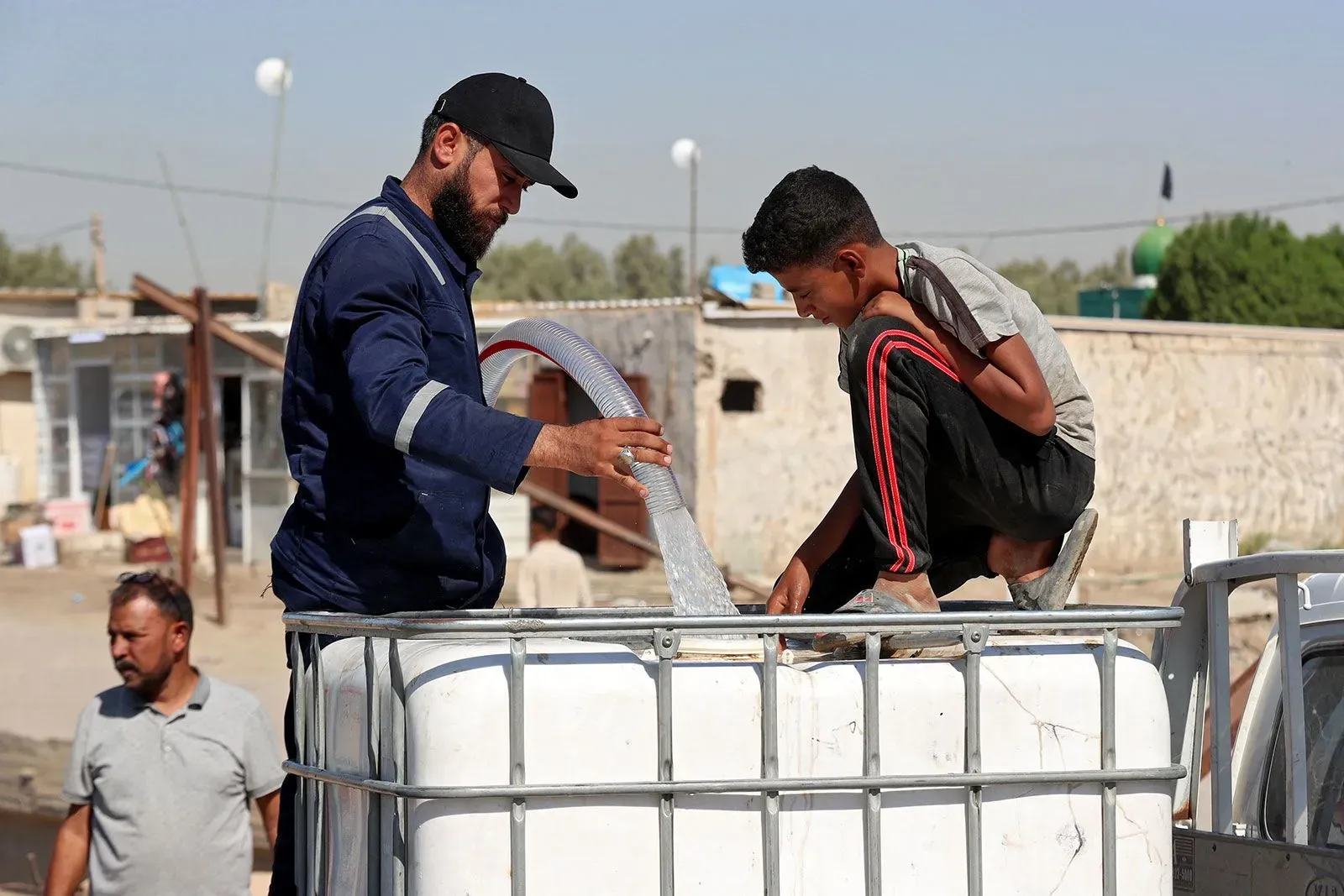 رجل وطفل يقومان بتعبئة المياه في حاوية كبيرة، وسط أجواء جافة تعكس أزمة المياه في العراق.