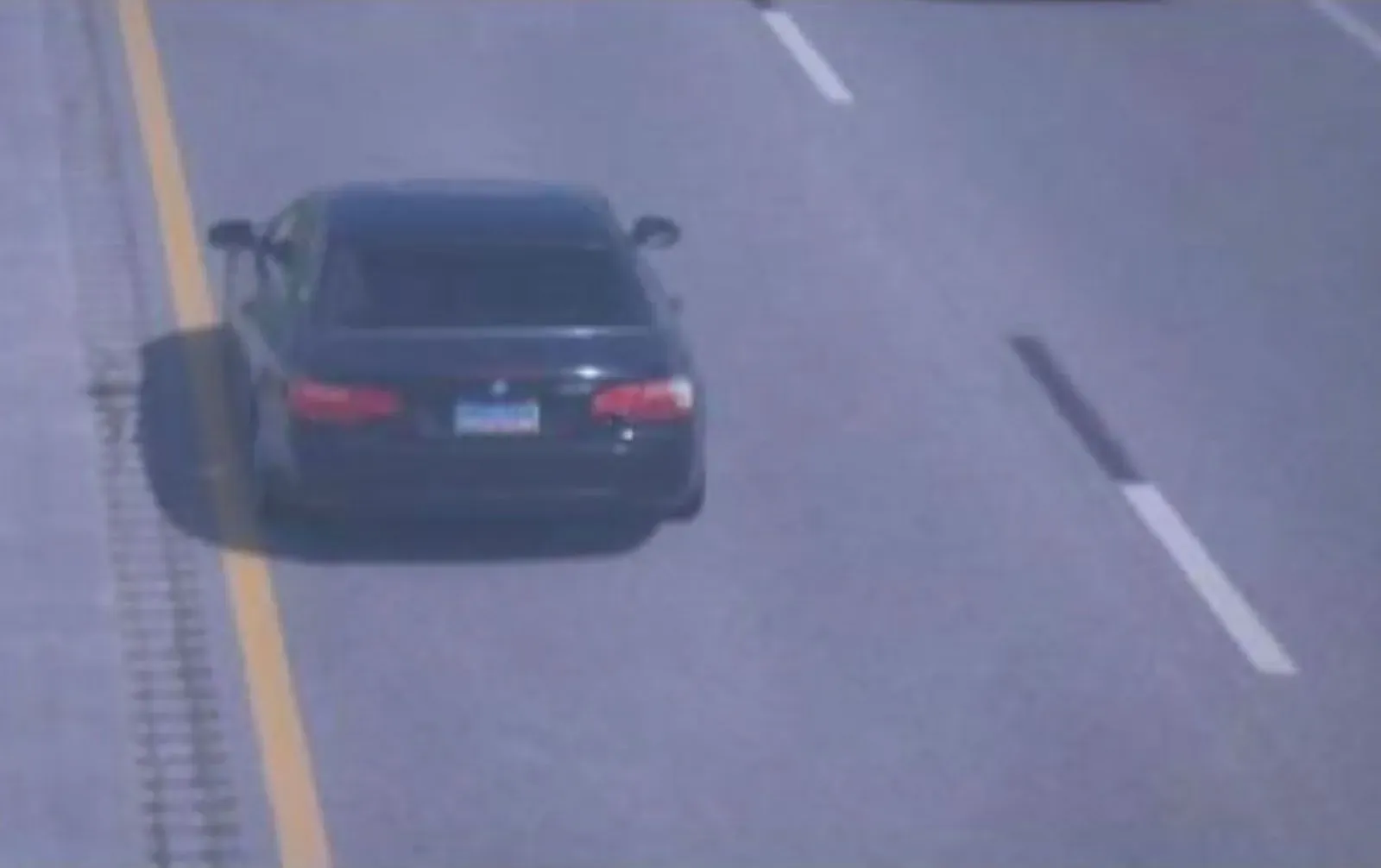 سيارة سوداء من طراز BMW تسير على الطريق السريع، مع وجود مسار متقطع على اليمين، مما يشير إلى حالة غير طبيعية أو خطر محتمل.