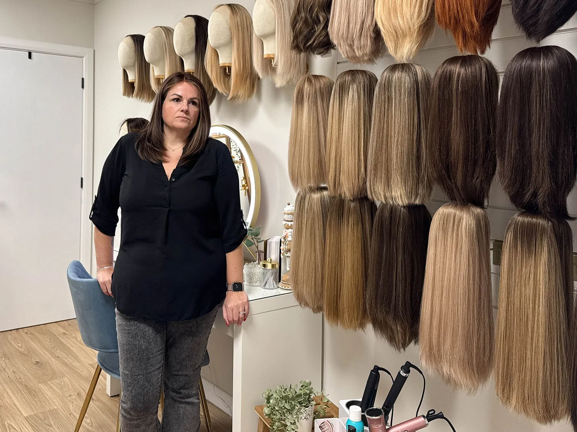 امرأة واقفة أمام مجموعة من الشعر المستعار بألوان وأطوال مختلفة، تعكس تحديات تساقط الشعر التي تواجهها النساء.