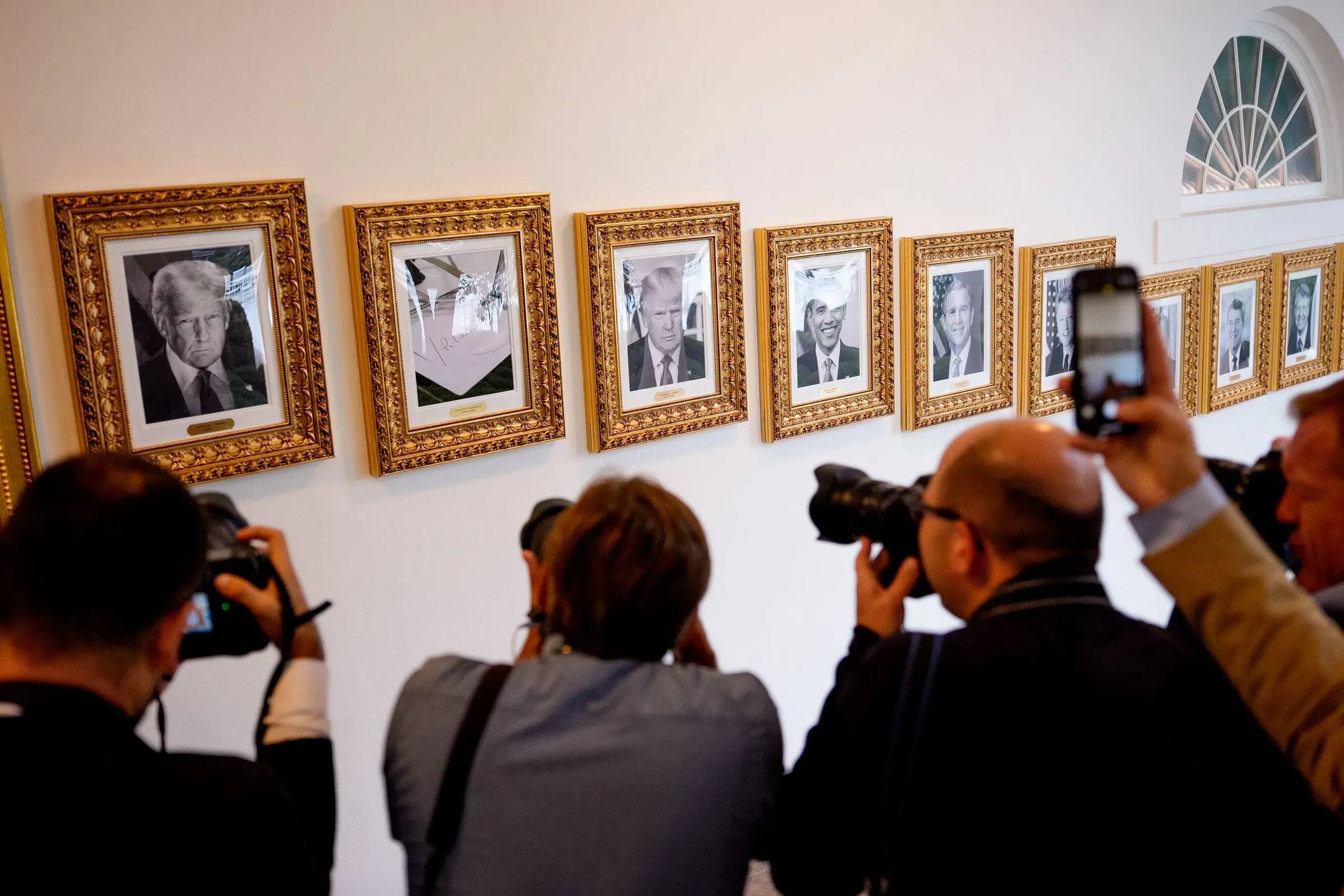 صور لعدد من الإطارات الذهبية التي تحتوي على صور للرؤساء الأمريكيين، مع وجود مصورين يلتقطون الصور.