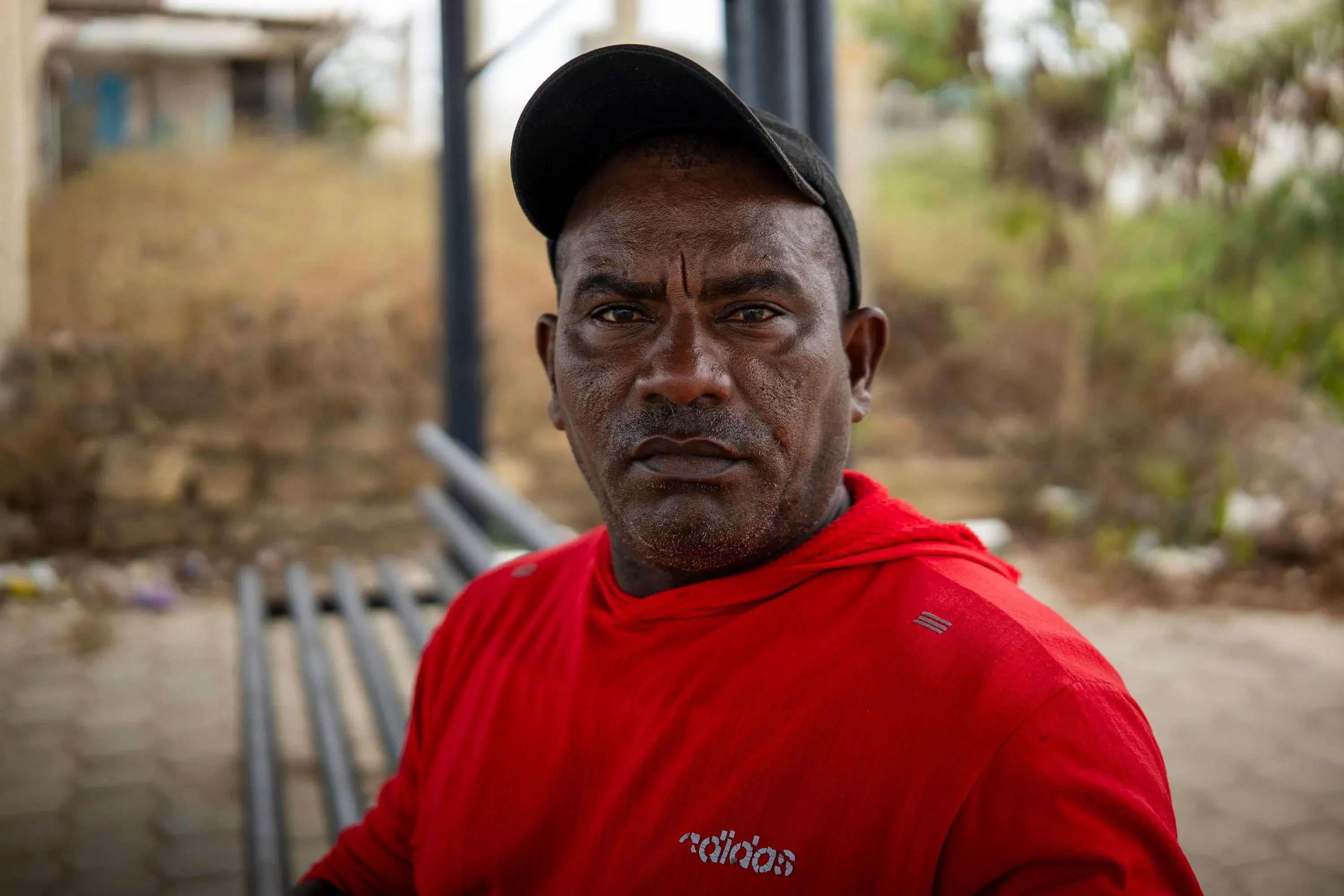 رجل يرتدي سترة حمراء وقبعة، يجلس في منطقة مفتوحة، مع تعبير جاد على وجهه، يعكس التحديات التي تواجه المجتمع في الإكوادور.