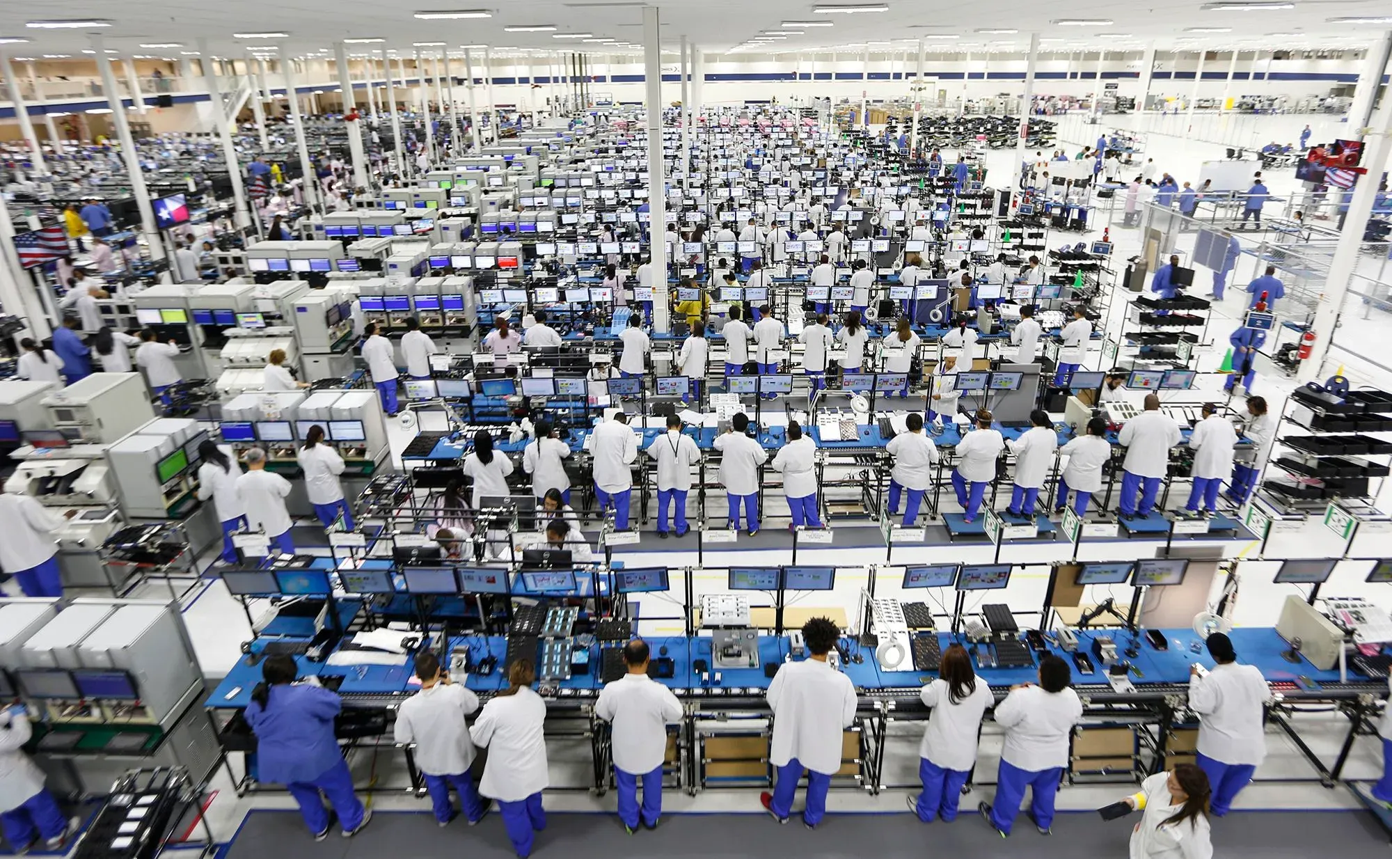 صورة لمصنع تجميع الهواتف الذكية، حيث يظهر عدد كبير من العمال يرتدون ملابس بيضاء، يعملون على خطوط الإنتاج.