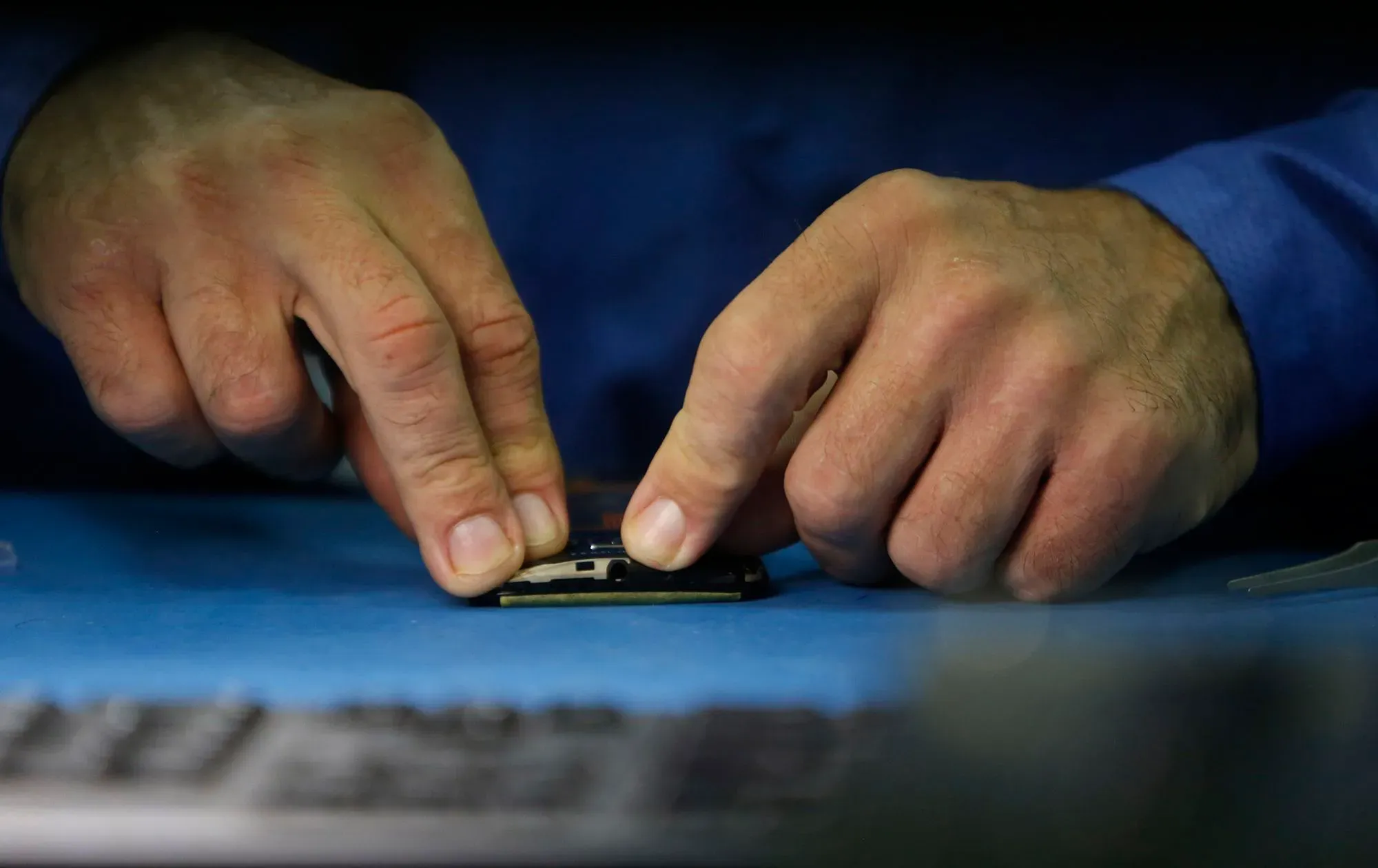 يد تظهر يدين تعملان على تجميع مكونات هاتف ذكي على سطح عمل أزرق، مما يعكس جهود موتورولا في تصنيع الهواتف في الولايات المتحدة.