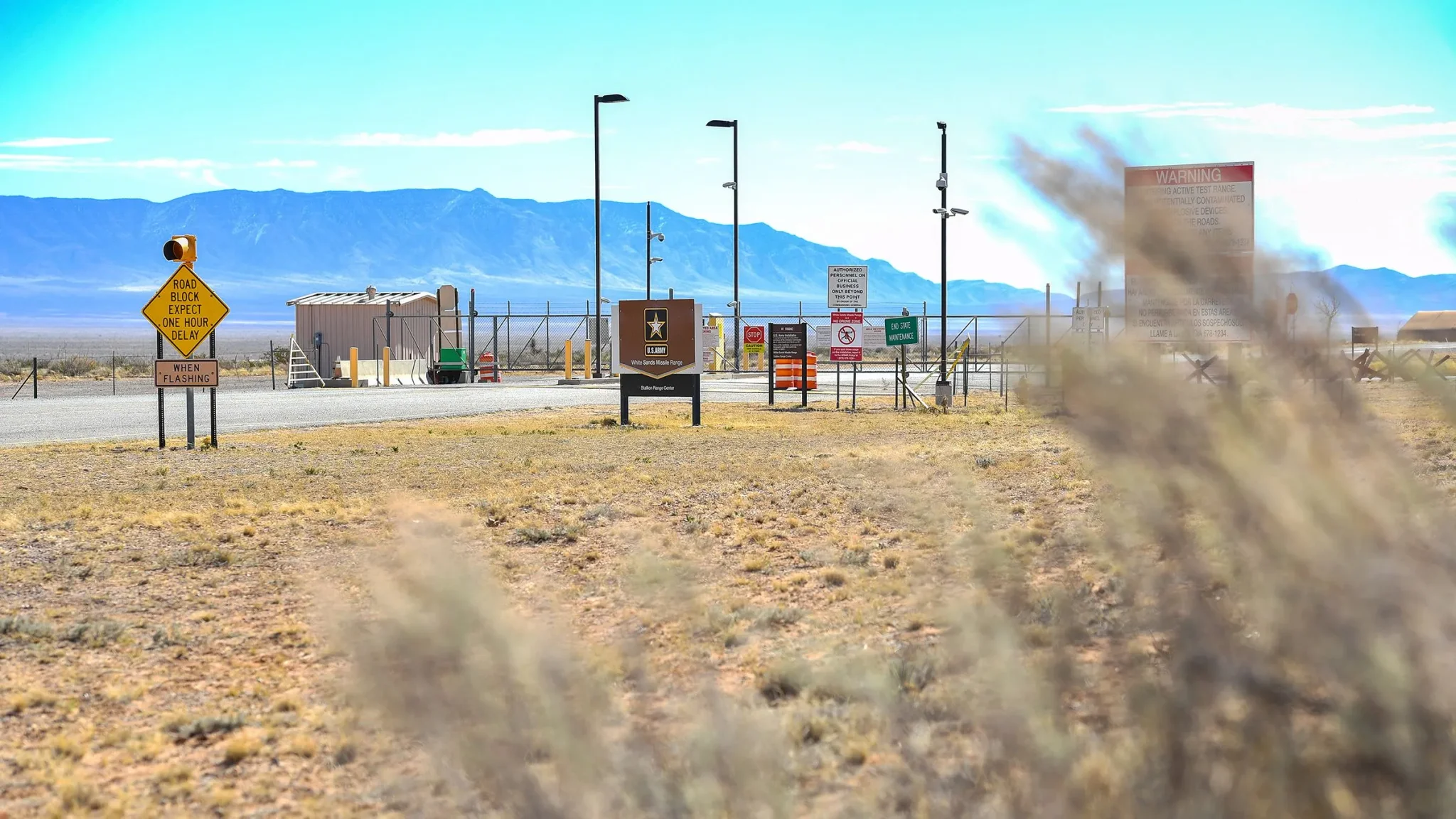 مدخل منشأة White Sands Missile Range العسكرية في نيو مكسيكو وسط صحراء وجبال، مع لافتات تحذيرية تعكس أهمية الموقع الأمني.