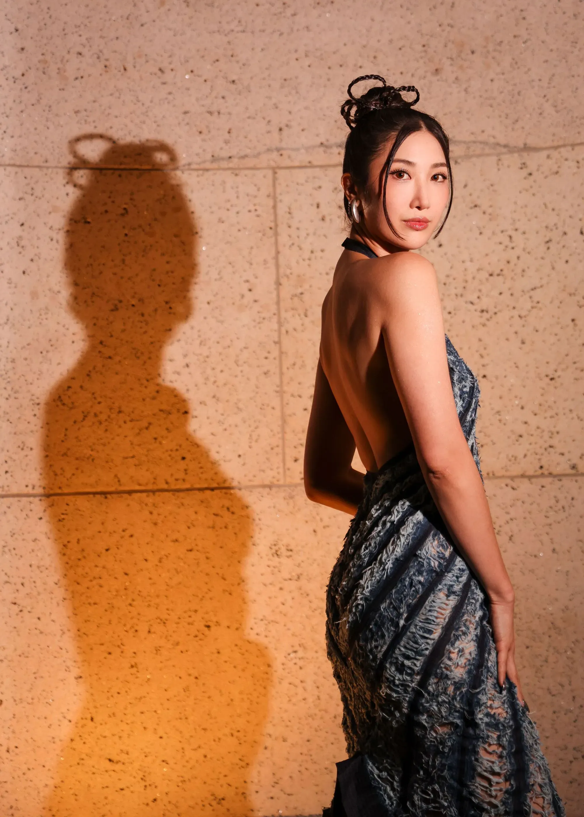 إيجاي ترتدي فستانًا أنيقًا وتظهر من الجانب، مع تسريحة شعر مميزة، بينما تلقي بظلالها على الجدار خلفها، تعكس نجاحها في عالم البوب الكوري.