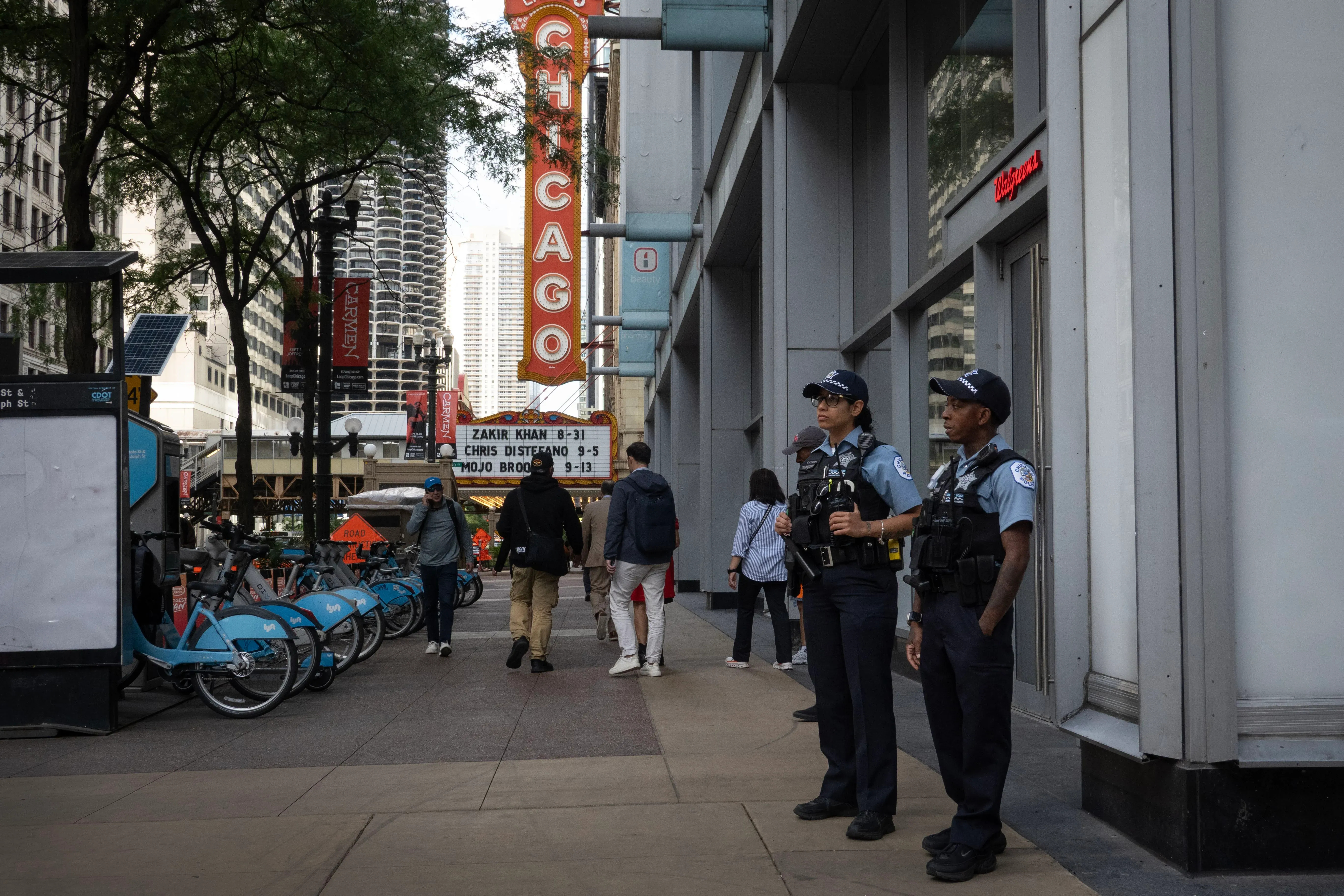شرطيان من إدارة شرطة شيكاغو يقفان في شارع مزدحم، مع وجود لافتة كبيرة تحمل اسم المدينة في الخلفية، في ظل توترات حول انتشار الحرس الوطني.