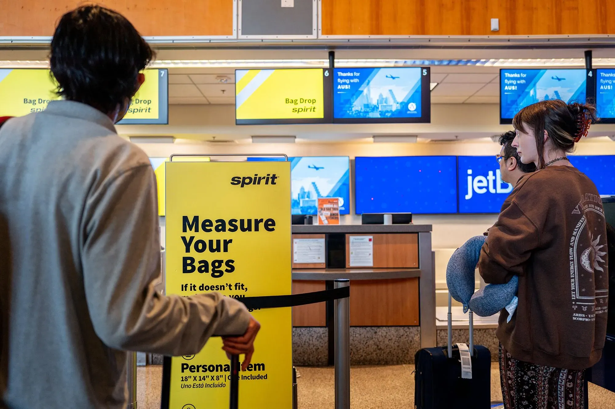 مكتب تسجيل الوصول لشركة Spirit Airlines مع لافتة تطلب من الركاب قياس أمتعتهم، بينما ينتظر المسافرون في الطابور.