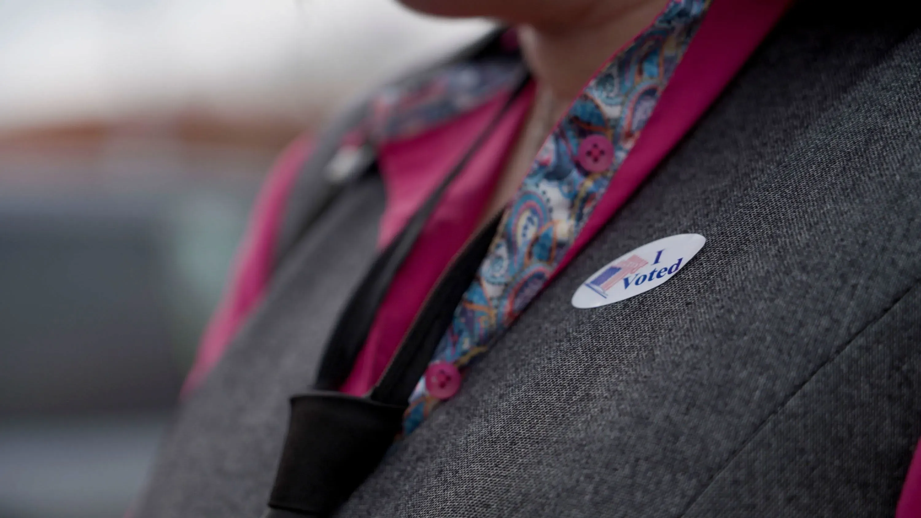 امرأة ترتدي سترة رمادية وقميصًا ورديًا، تحمل ملصق "صوتت" على صدرها، في موقف سيارات مكتبة خلال يوم التصويت المبكر في أركنساس.