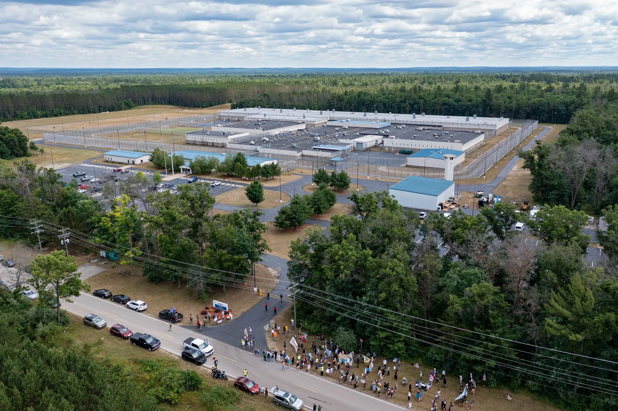 صورة جوية لمركز احتجاز كبير محاط بالأشجار، يظهر فيه تجمع للناس أمام المدخل، مما يعكس قضايا الهجرة والاحتجاز في الولايات المتحدة.