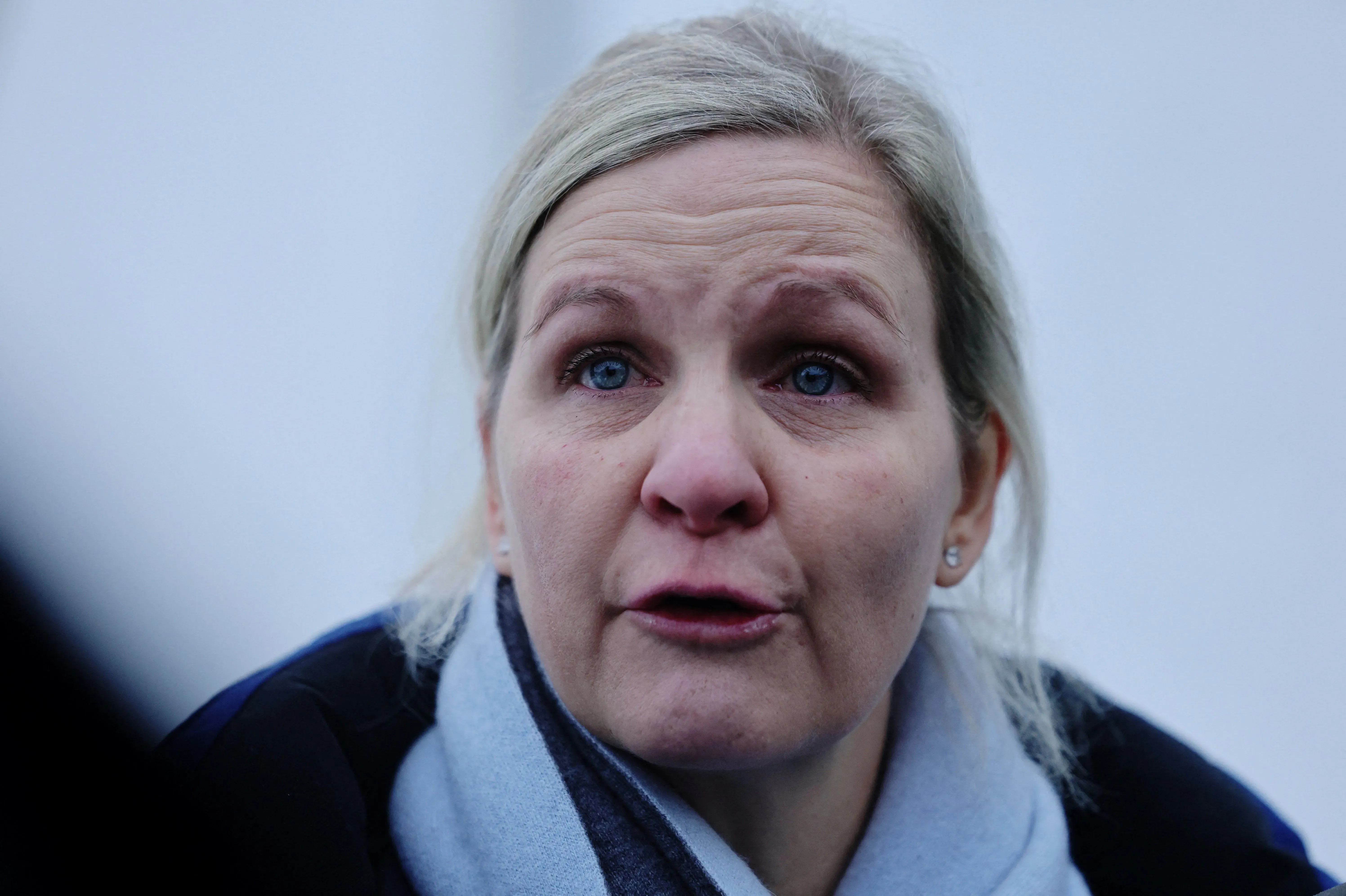 امرأة تعبر عن مشاعرها في مركز كورتينا، تحمل شارة سوداء وتظهر تأثرها بسبب استبعاد المتزلج الأوكراني هراسكيفيتش من الأولمبياد.