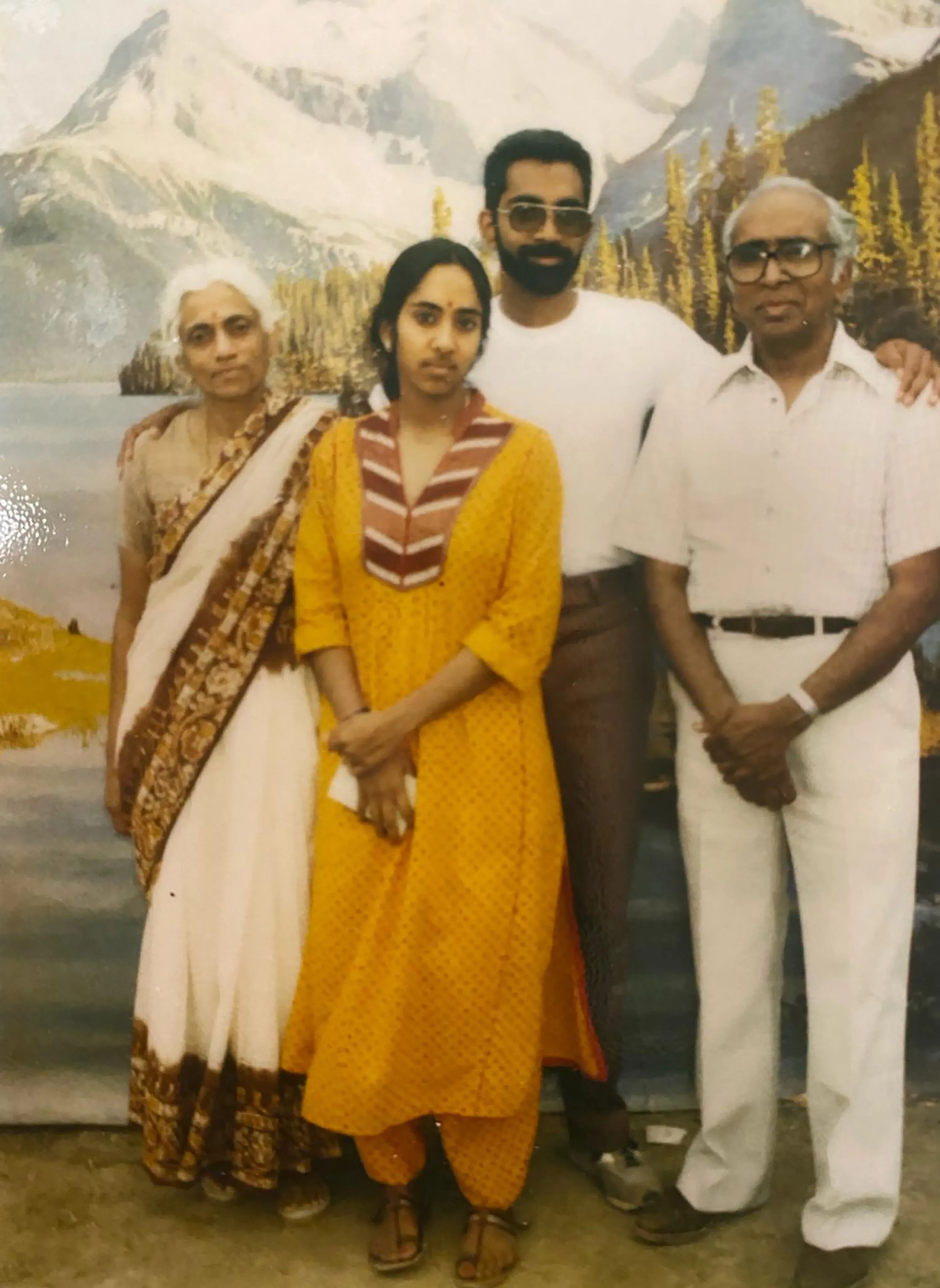 صورة لعائلة تتكون من أربعة أفراد، بينهم امرأة ترتدي زيًا تقليديًا أصفر ورجل يرتدي نظارات شمسية، يقفون أمام منظر طبيعي جبلي.