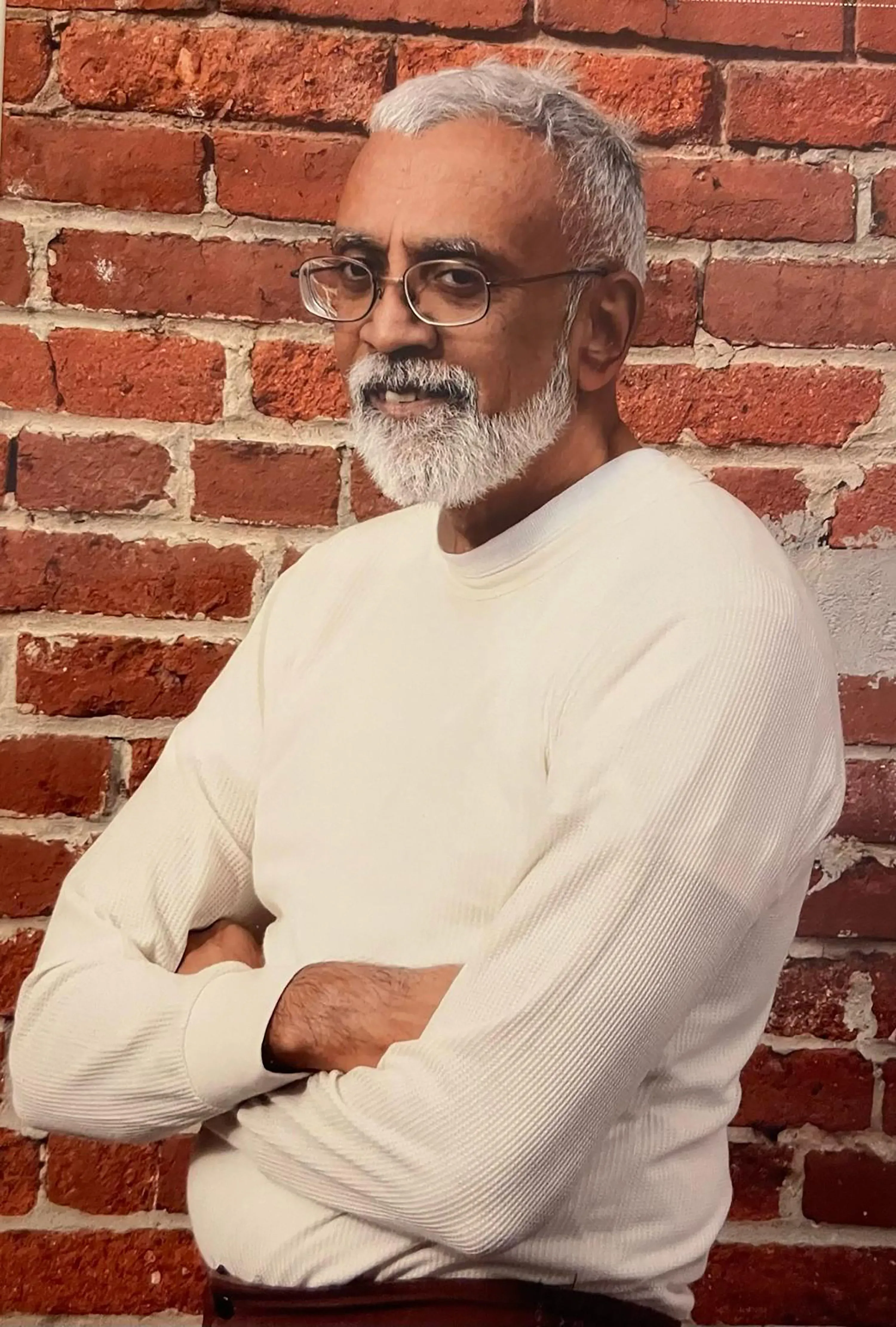 صورة لرجل مسن ذو لحية وشعر رمادي، يرتدي قميصًا أبيض، يقف مع ذراعيه متقاطعتين أمام جدار من الطوب الأحمر. تعكس تعابيره الأمل والتفاؤل بعد إلغاء إدانته بالقتل.