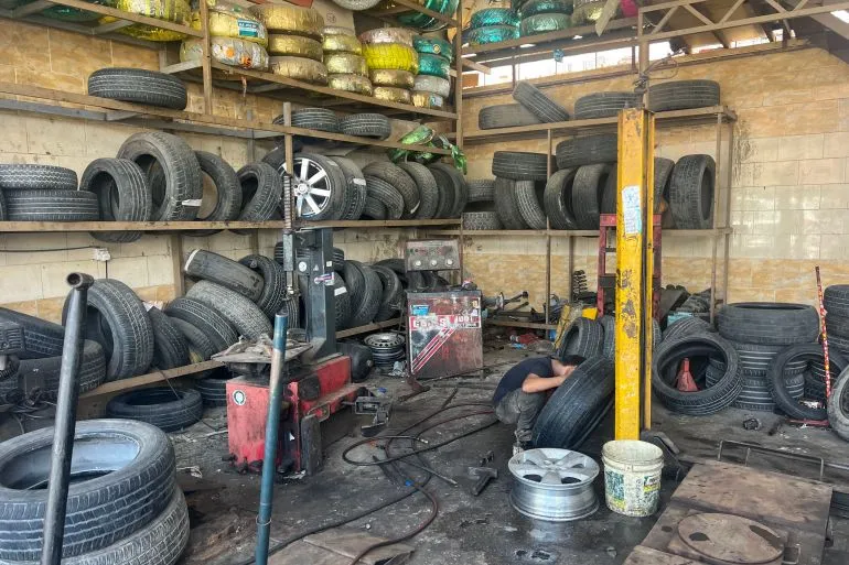 ورشة لتصليح الإطارات في اليمن، حيث يعمل عامل على إصلاح إطار وسط فوضى من الإطارات القديمة، تعكس تأثير انقطاع الكهرباء على الأعمال.
