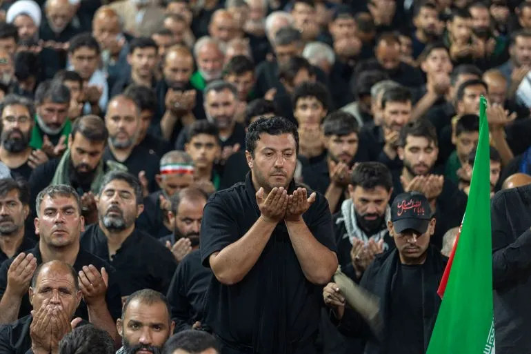 رجال إيرانيون يرتدون الأسود يؤدون صلاة جماعية في مراسم تشييع علي خامنئي وسط أجواء حزينة وتعكس التوترات السياسية في إيران.