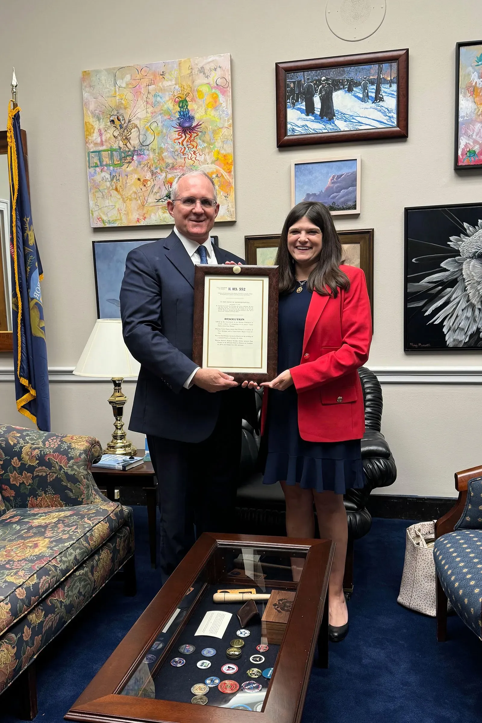 بول ويلان مع نائبة الكونغرس ديبي دينجل، يحملان وثيقة رسمية في مكتبها، وسط لوحات فنية وأثاث مريح، في سياق جهود دعم السجناء السابقين.