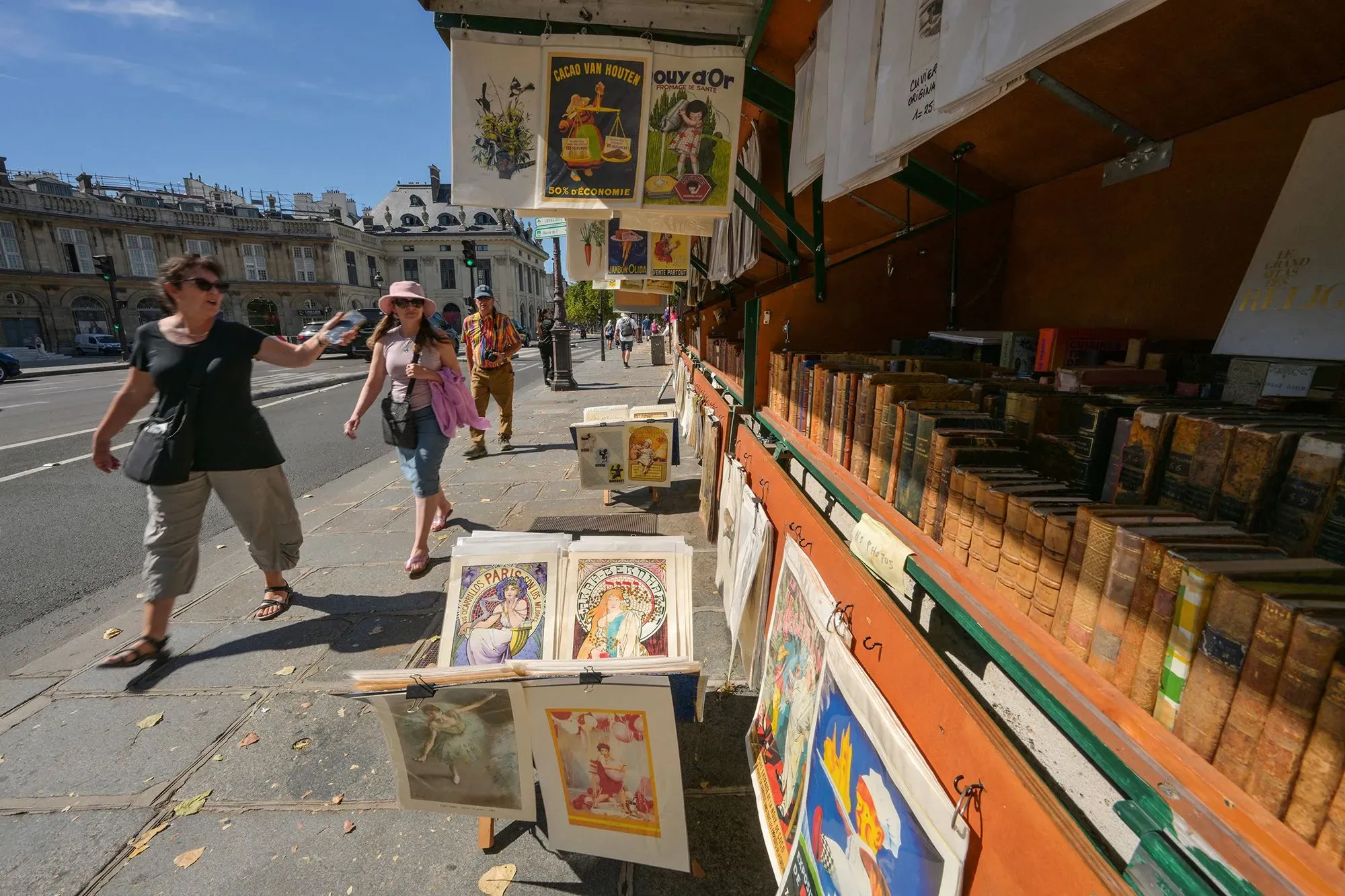 باعة الكتب في باريس يعرضون كتبًا قديمة ومعاصرة في أكشاك على ضفاف نهر السين، مع إطلالة على المباني التاريخية.
