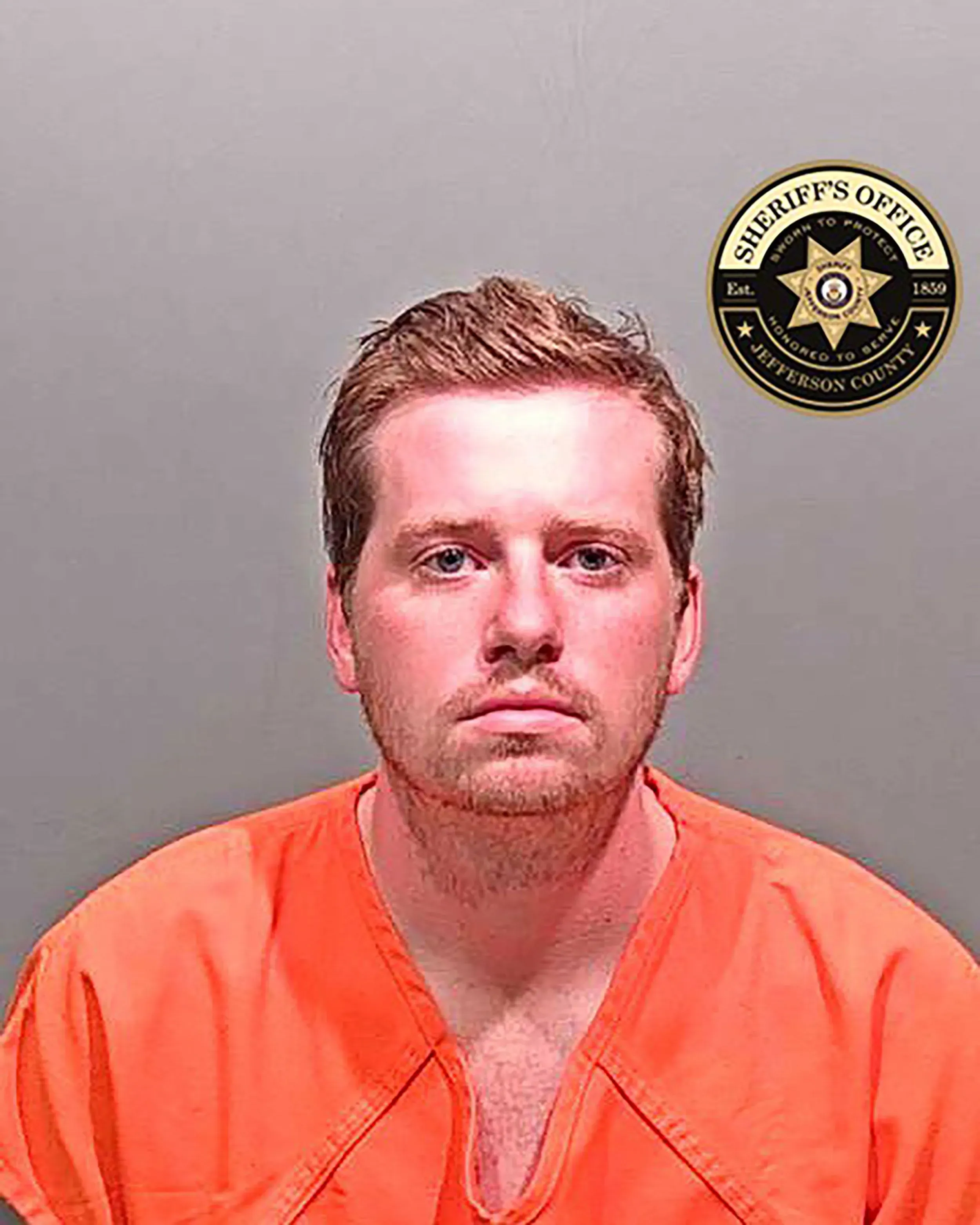 صورة لمشتبه به يرتدي زي السجن البرتقالي، يظهر بملامح جادة، مع شعار مكتب الشريف في الزاوية.