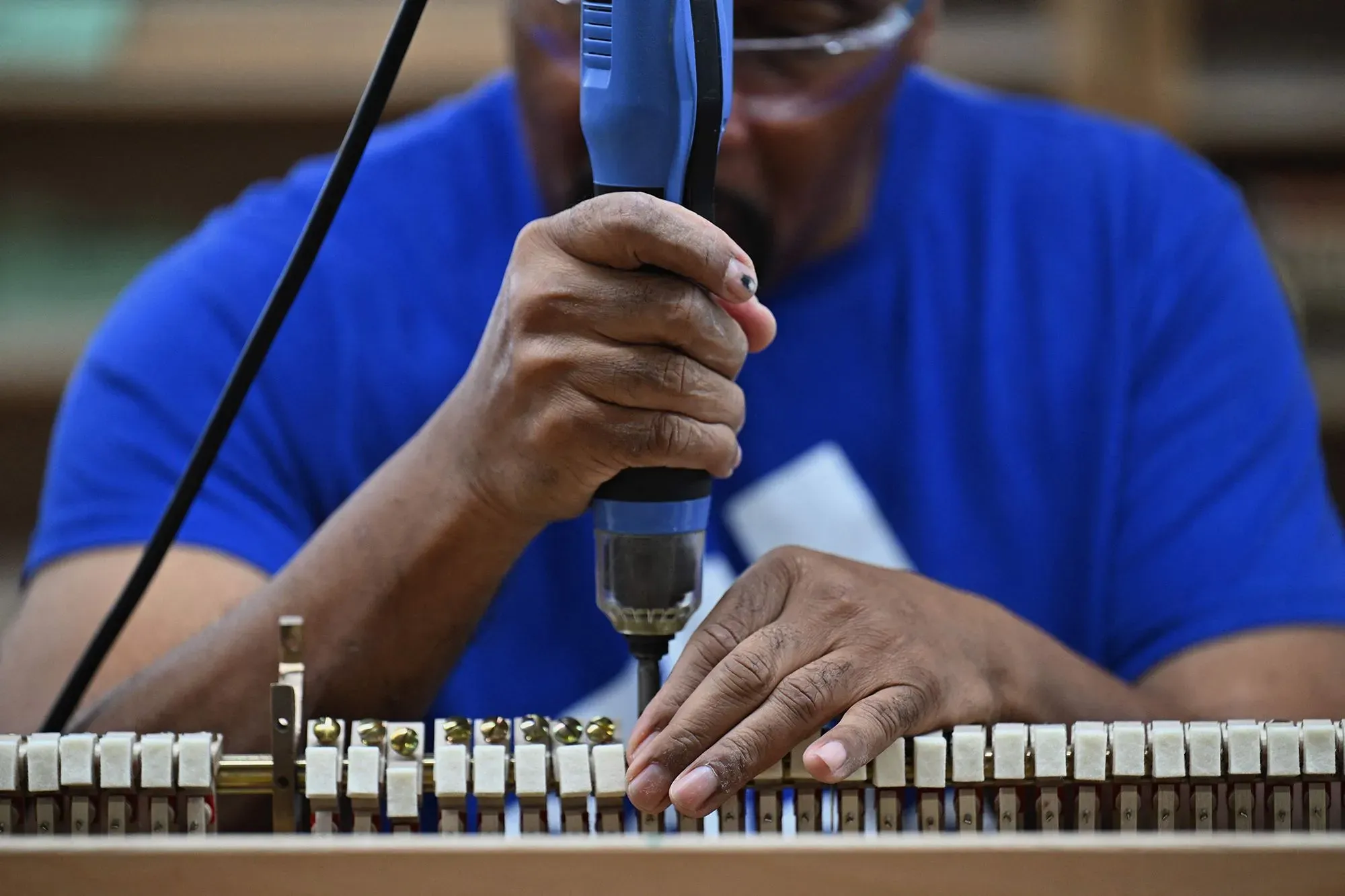عامل يستخدم مثقابًا كهربائيًا لتثبيت مكونات البيانو في مصنع شتاينواي، مع التركيز على الحرفية الدقيقة في صناعة الآلات الموسيقية.