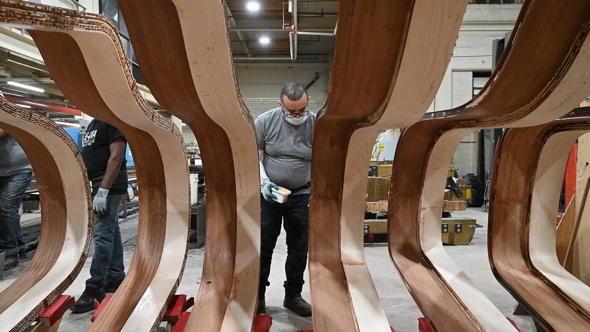 عمال في مصنع شتاينواي يقومون بتشكيل هياكل البيانو من الخشب، مع التركيز على الجودة والحرفية في عملية التصنيع.