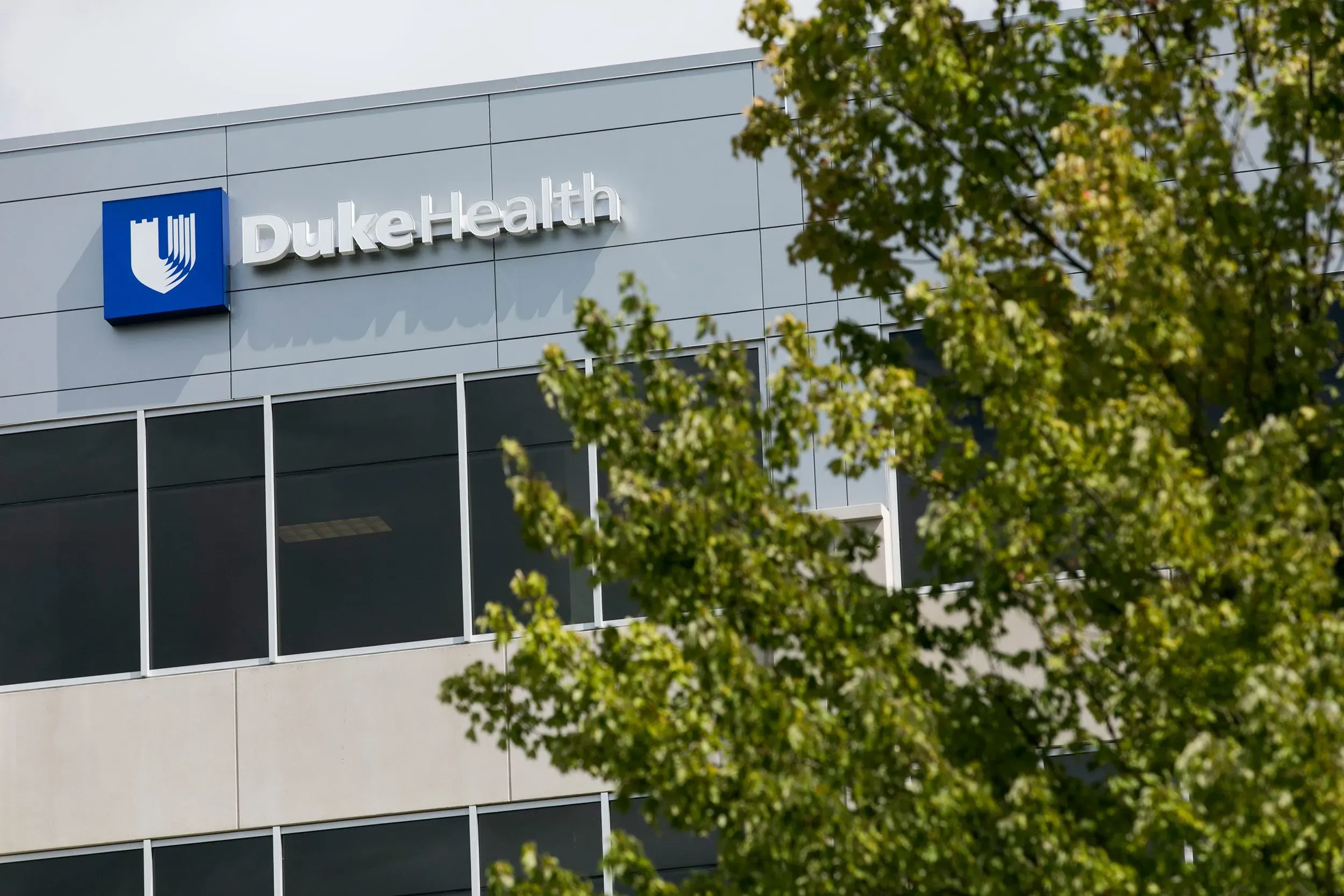 واجهة مستشفى جامعة ديوك، مع شعار Duke Health، محاطة بأشجار خضراء، تشير إلى دور المستشفى في تقديم الرعاية الصحية المتقدمة.