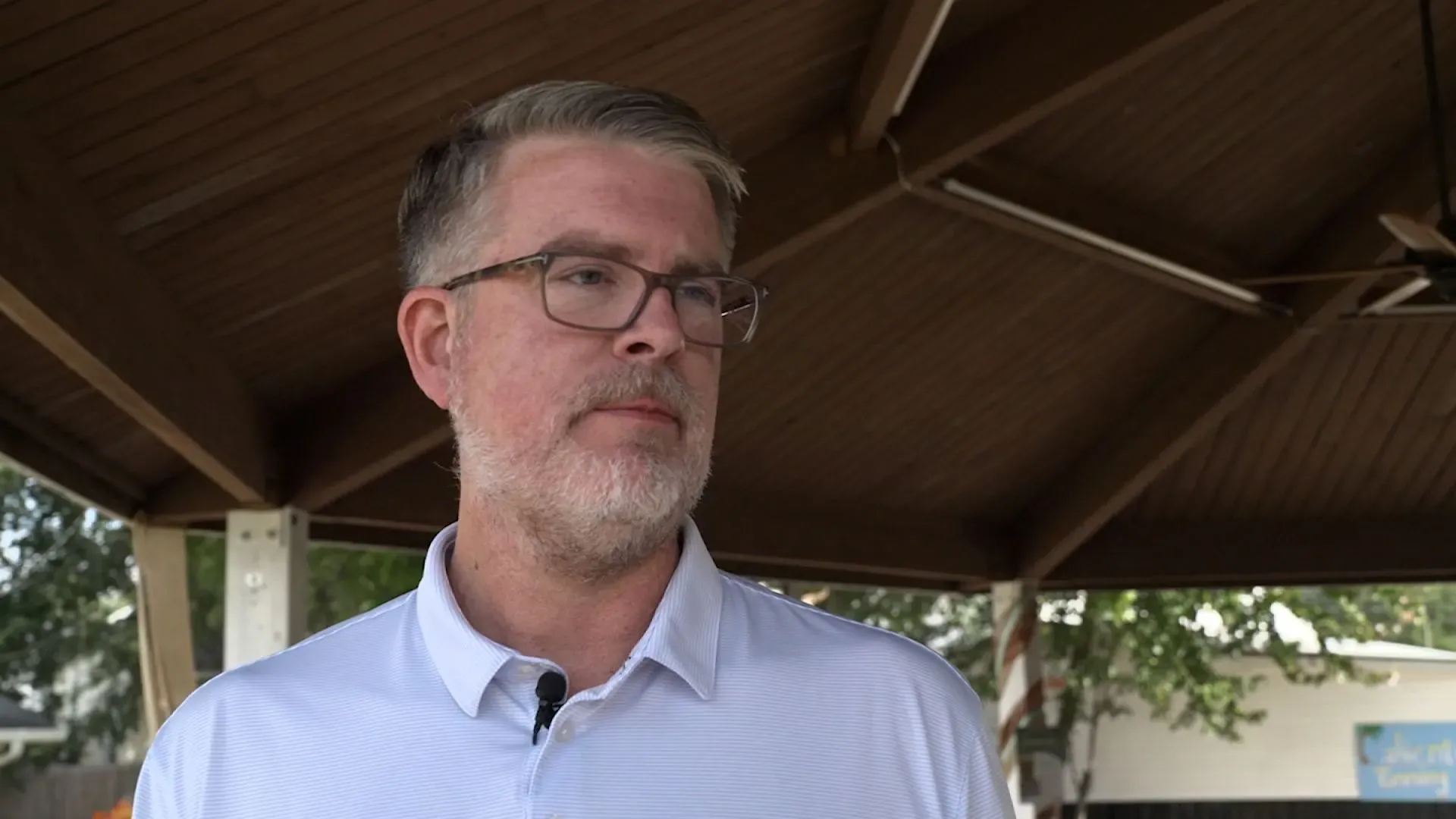 رجل يرتدي نظارات وقميصًا أبيض، يبدو متفكرًا في مكان مفتوح تحت سقف خشبي، مما يعكس موضوع البحث عن التاريخ الصحي العائلي.