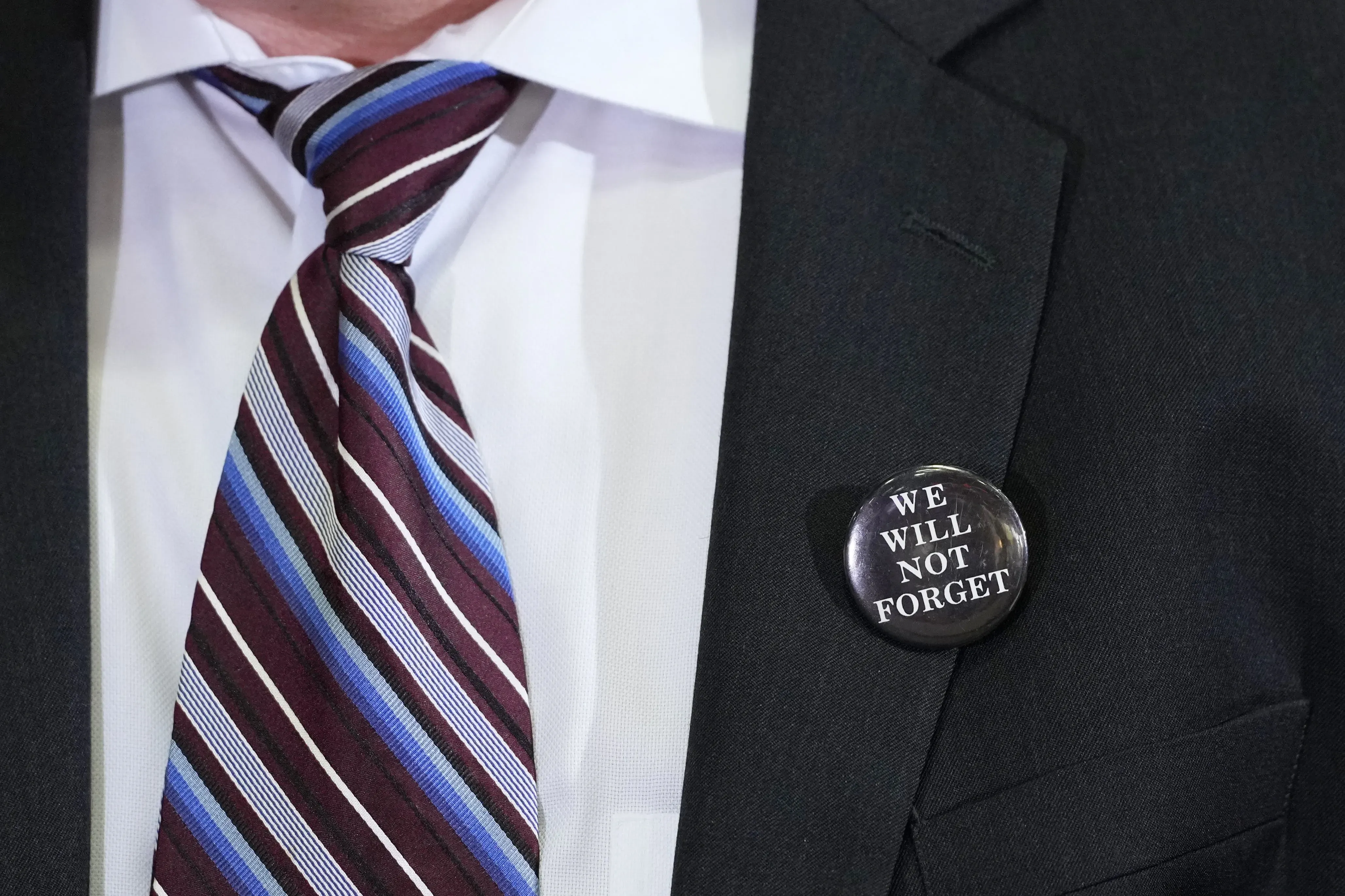 شارة تحمل عبارة "لن ننسى" مثبتة على صدر شخص يرتدي بدلة، تعبيرًا عن التزامه بحل قضية جرائم قتل الفتيات الأربع في أوستن.