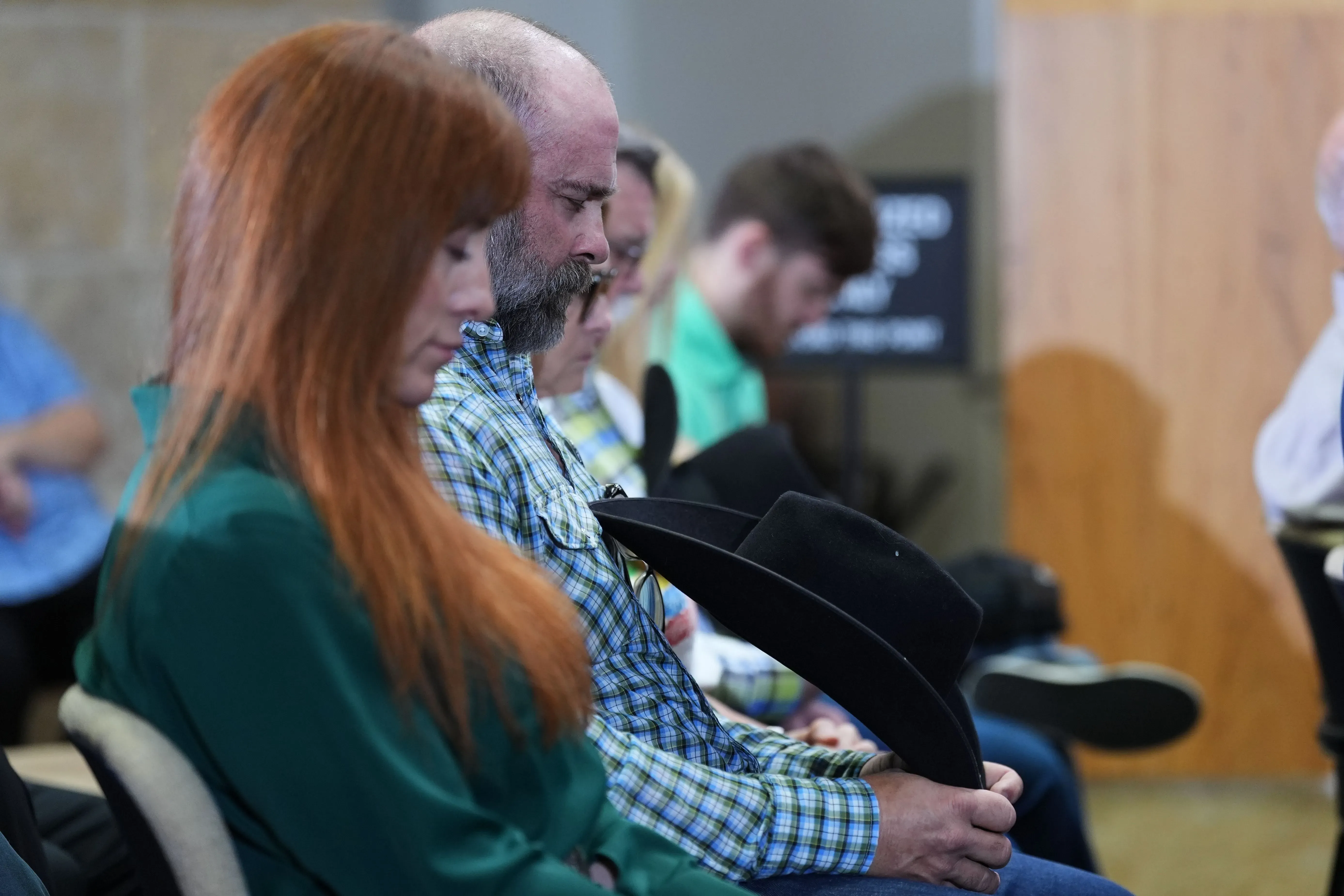 أشخاص يجلسون في قاعة، بعضهم يحمل قبعات، في لحظة تأمل خلال مؤتمر صحفي حول حل قضية جرائم قتل الفتيات الأربع في أوستن.