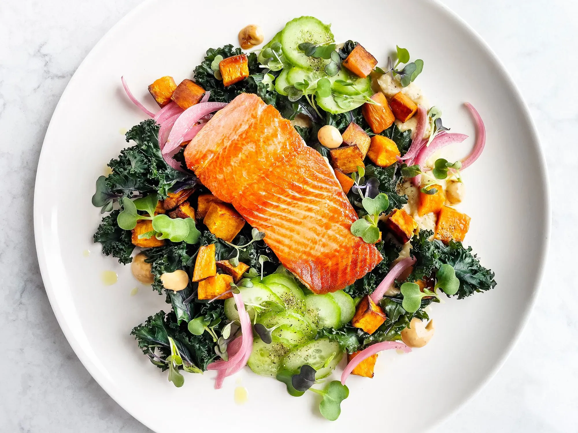 طبق صحي يحتوي على سمك السلمون المشوي مع خضروات متنوعة مثل الكيل والبطاطا الحلوة والخيار، يعكس أهمية التغذية لصحة العظام.