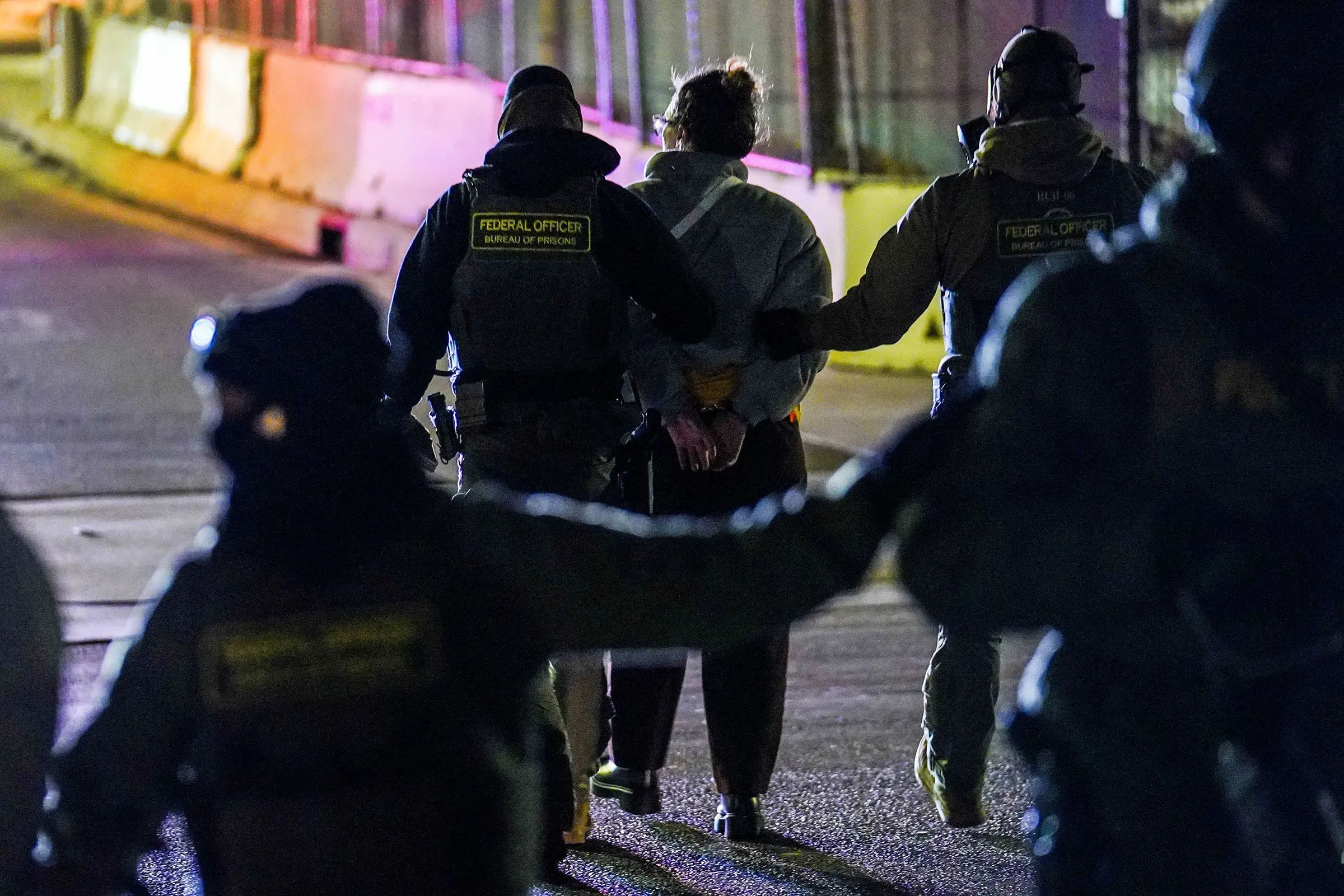 ضباط فيدراليون يرتدون معدات تكتيكية يعتقلون شخصًا في مينيابوليس، بينما يتظاهر حشد ضد إجراءات الهجرة.