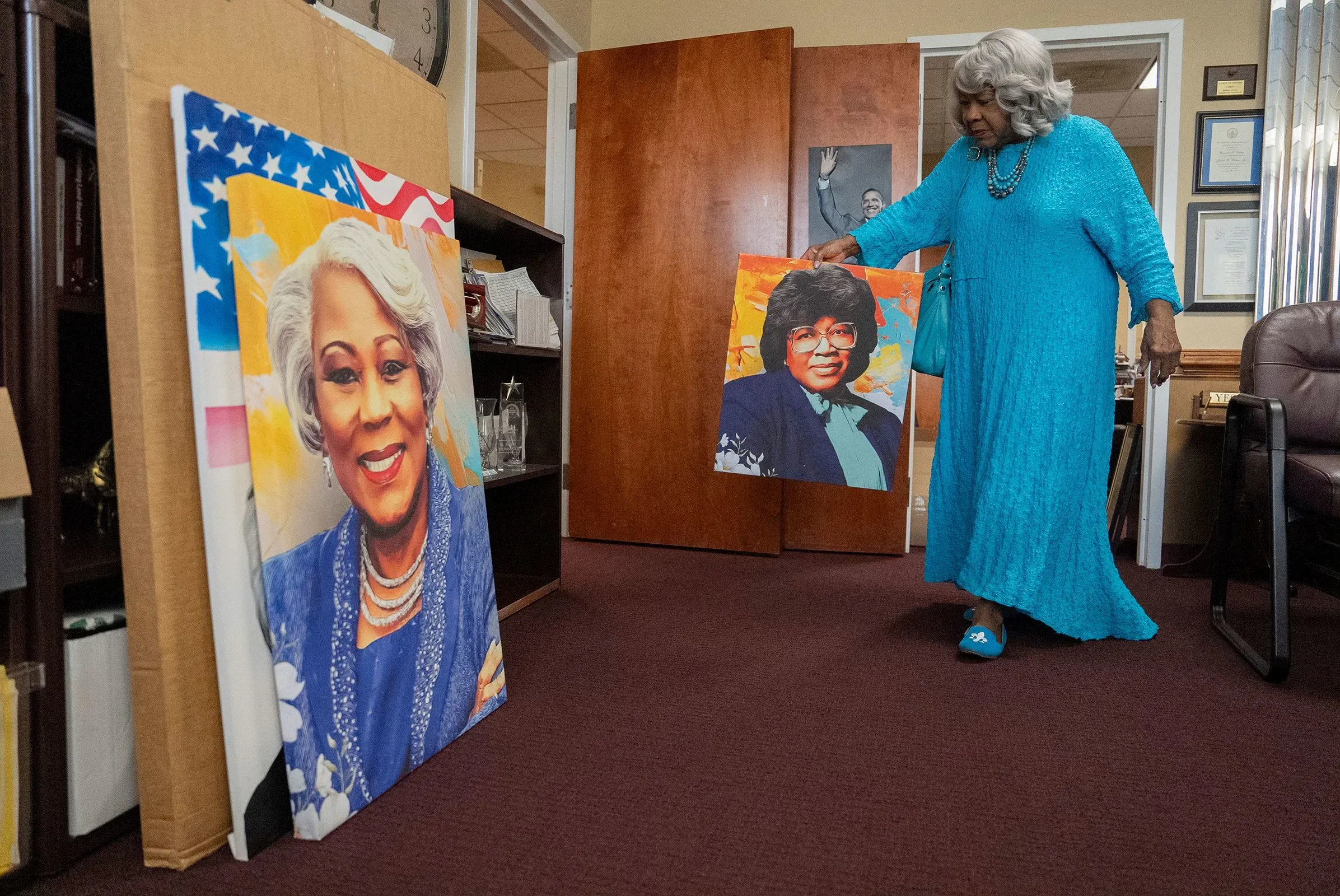 امرأة مسنّة ترتدي فستانًا أزرق وتحمل صورة ملونة لنفسها في شبابها، بينما توجد صور أخرى ملصقة بالقرب منها.