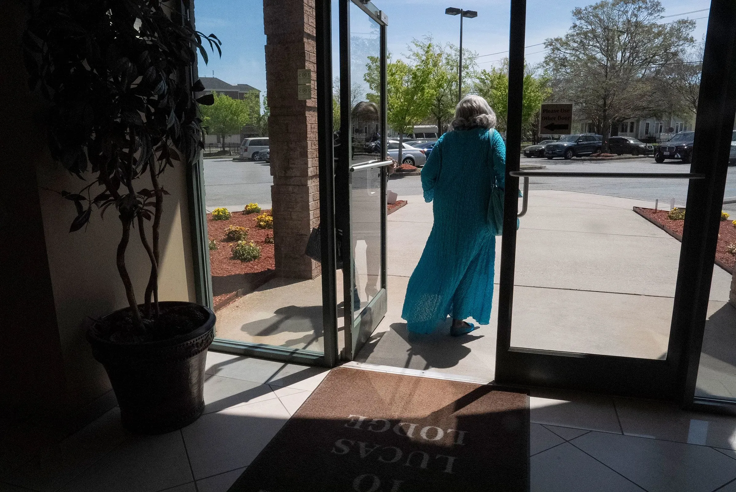 امرأة مسنّة ترتدي ثوبًا أزرق وتخرج من مبنى، مع تفاصيل طبيعية واضحة في الخلفية، تعكس نشاطها السياسي في فرجينيا.