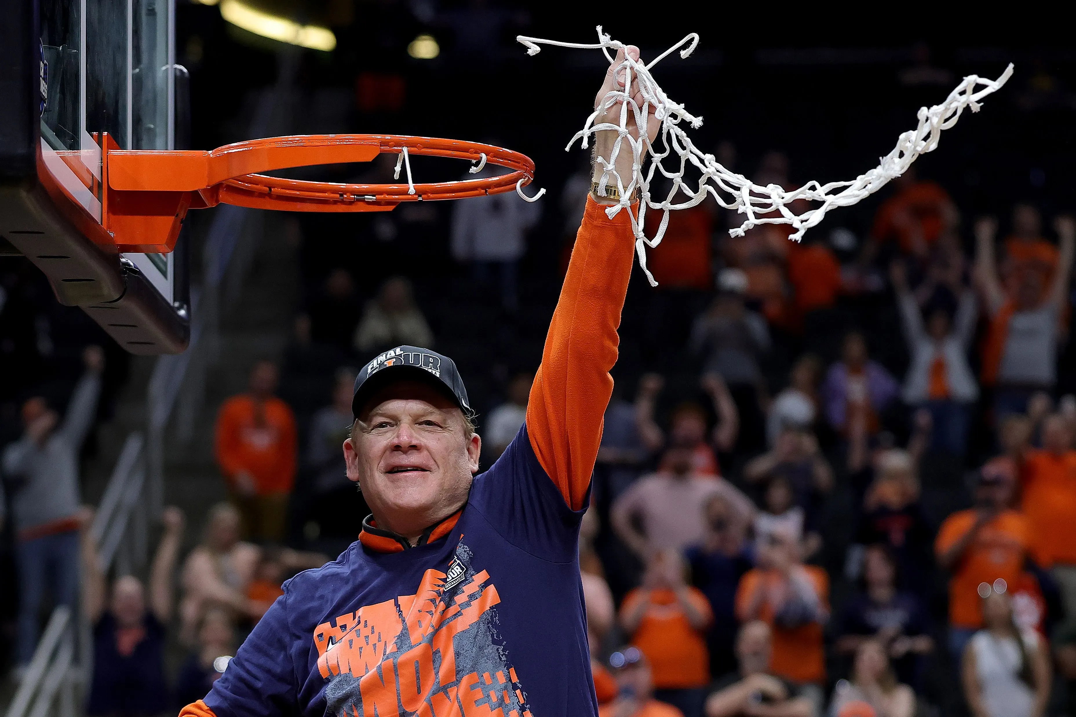 مدرب كرة السلة براد أندروود يحتفل بفوز فريقه بعد قطع الشبكة، مع جمهور متحمس في الخلفية، مشيرًا إلى نجاح برنامج "بروفايل".