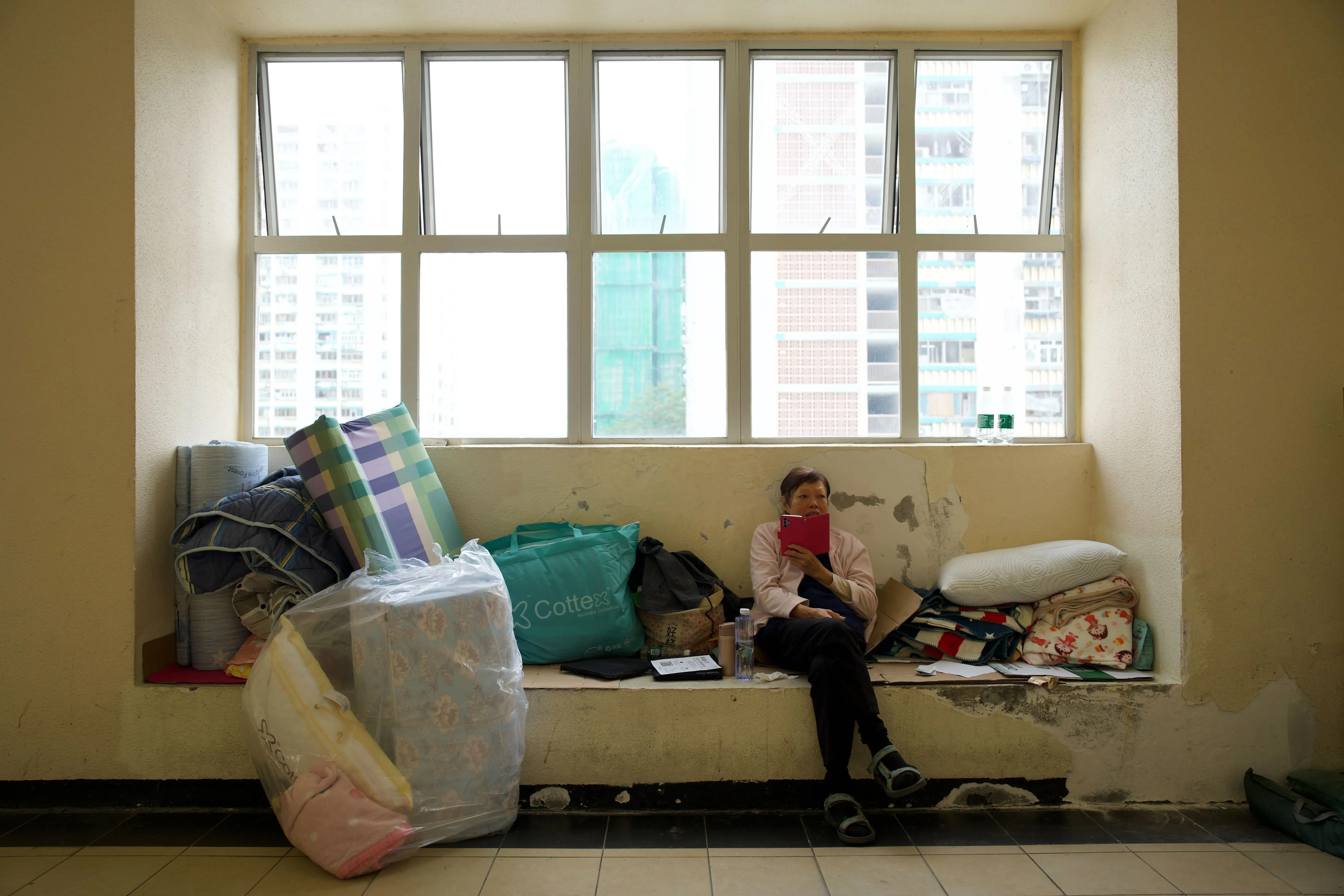 امرأة مسنّة تجلس على حافة نافذة في مجمع سكني بحالة فوضى، محاطة بأغراض شخصية، بعد الحريق المميت في هونغ كونغ.