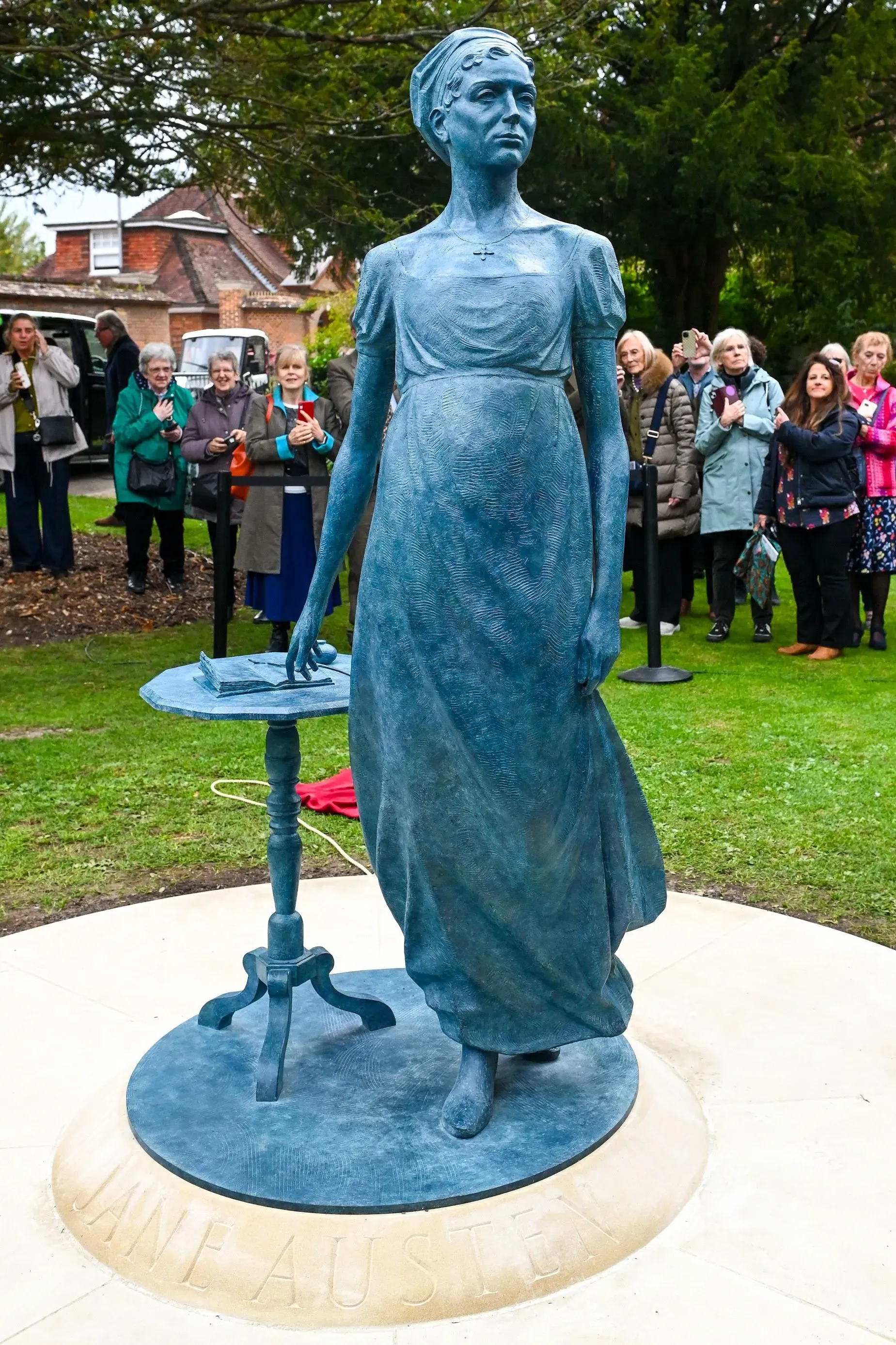 تمثال لجين أوستن في حديقة، يظهرها واقفة بجانب طاولة، مع حشد من المعجبين خلفها، احتفالاً بذكراها.