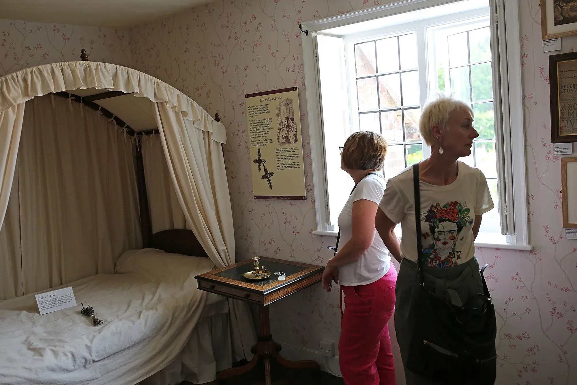 غرفة جين أوستن في منزلها، حيث زارت المعجبات المعرض، مع سرير مغطى وستائر بيضاء، وجدران مزينة بأزهار.