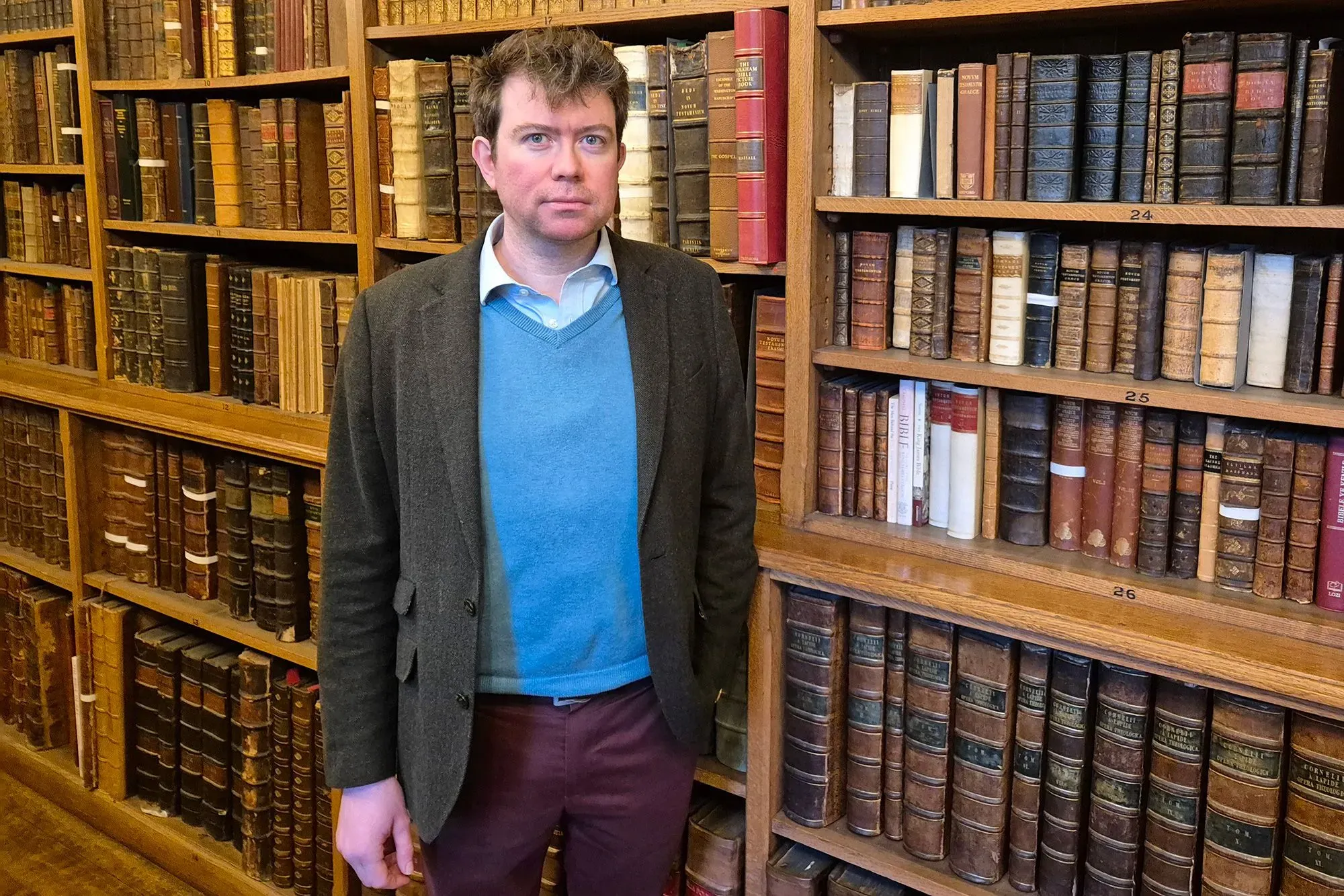 رجل يقف أمام رفوف مليئة بالكتب القديمة في مكتبة، تعكس اهتمامه بالأدب، خاصة أعمال جين أوستن.