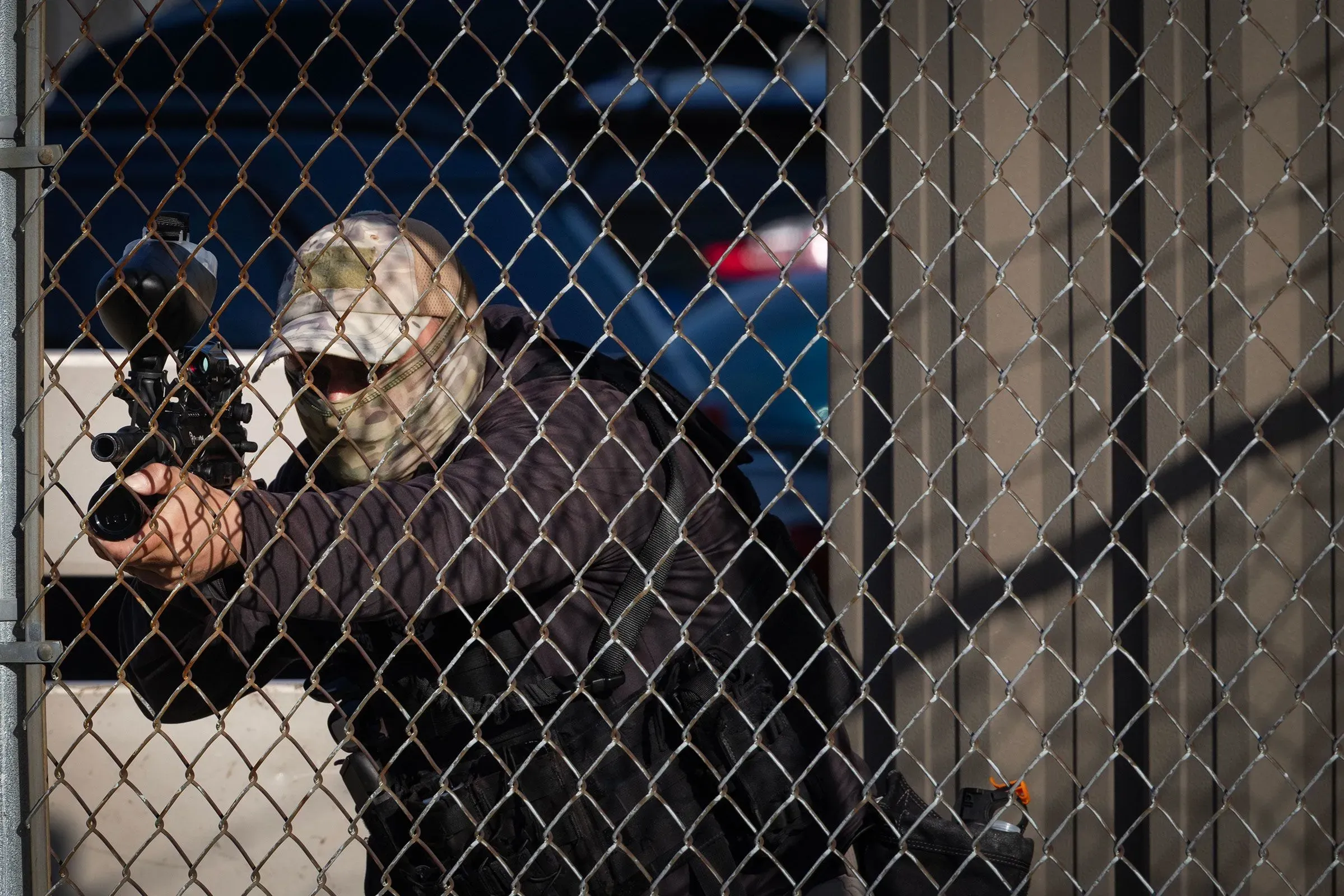 عميل فيدرالي يتخذ وضعية إطلاق نار خلف سياج معدني، ممسكًا بمسدس كرات الفلفل، في سياق مواجهة مع المتظاهرين في شيكاغو.