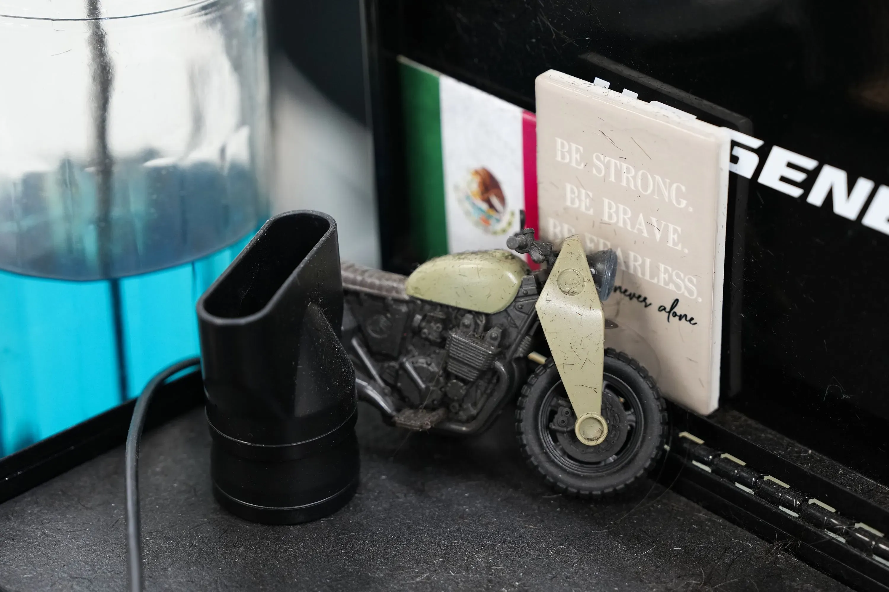 دراجة صغيرة رمادية اللون مع كتاب يحمل عبارة "كن قويًا، كن شجاعًا" وعلم مكسيكي، تعكس ثقافة المجتمع المحلي في استوديو الرقص.