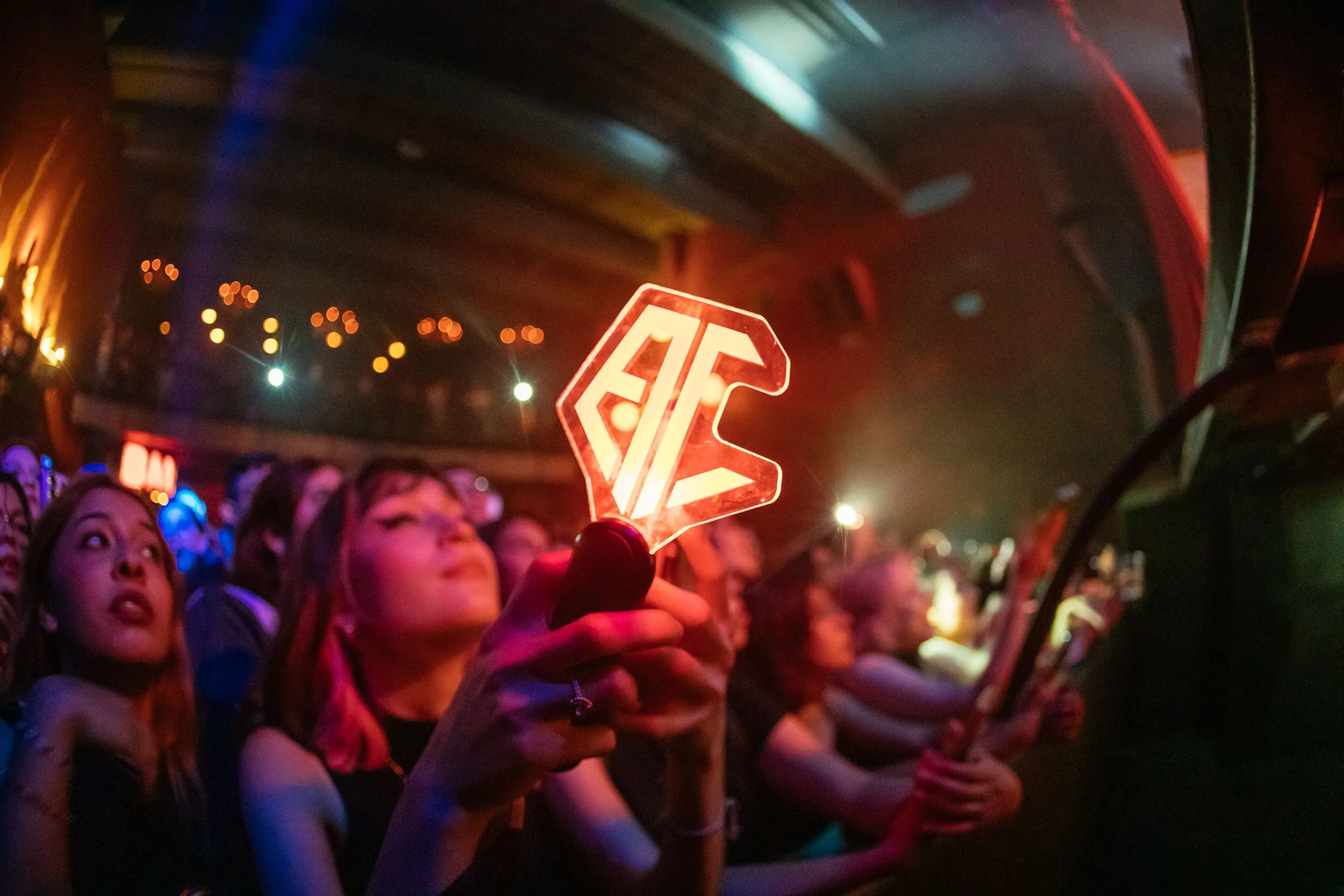 جمهور متحمس في حفل كيبوب، يحملون لافتات مضيئة تحمل شعار الفرقة، وسط أجواء احتفالية وعاطفية.