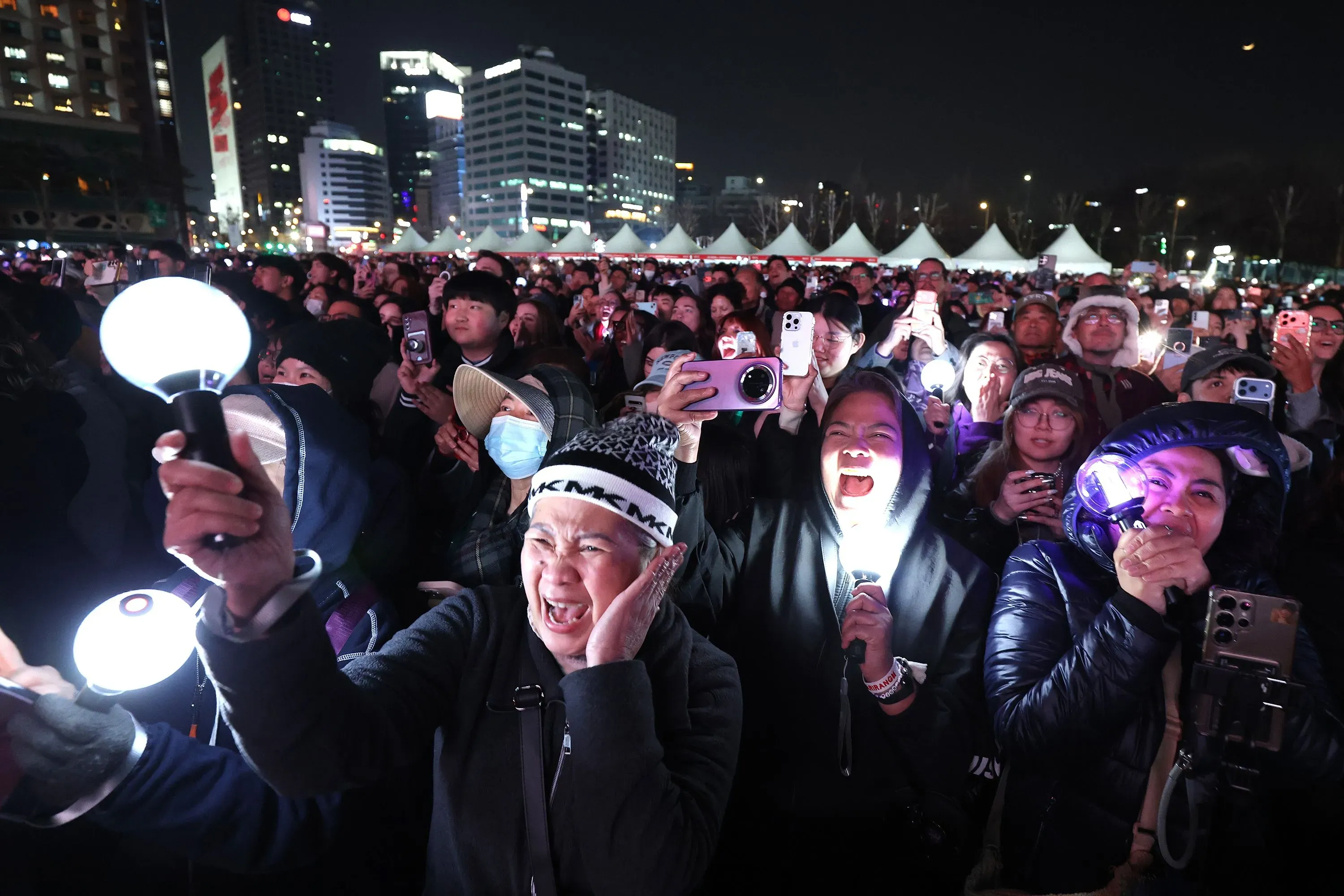 حشود من المعجبين في حفل موسيقي، يحملون مصابيح مضيئة ويعبرون عن حماسهم لفرقة BTS، مما يعكس شغف الكيبوب في أمريكا اللاتينية.