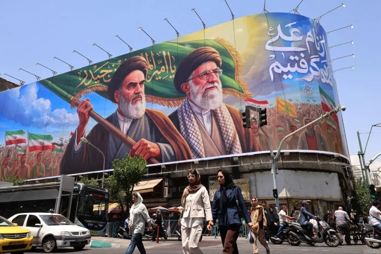 لوحة إعلانات كبيرة في طهران تُظهر شخصيات دينية بارزة، مع شعارات تدعو إلى المقاومة، بينما يمر الناس في الشارع.