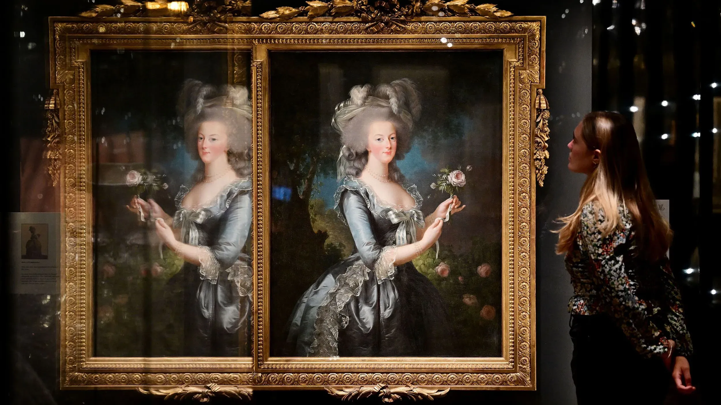 امرأة تنظر إلى لوحة تاريخية لماري أنطوانيت، ترتدي فستاناً أزرق مزيناً، وتحمل وردة، في معرض بمتحف فيكتوريا وألبرت.
